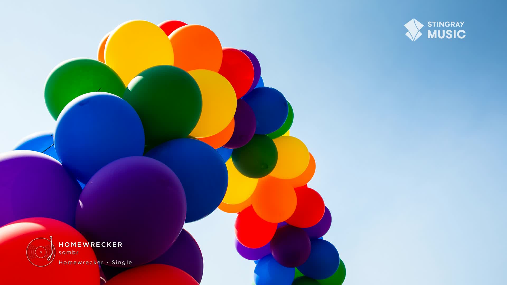 A vibrant arc of balloons, in shades of red, orange, yellow, green, blue, and purple, stretches across the bright blue sky. This display, reminiscent of a Pride celebration in Canada, is promoting the Stingray Hit List single "Homewrecker" by sombr.