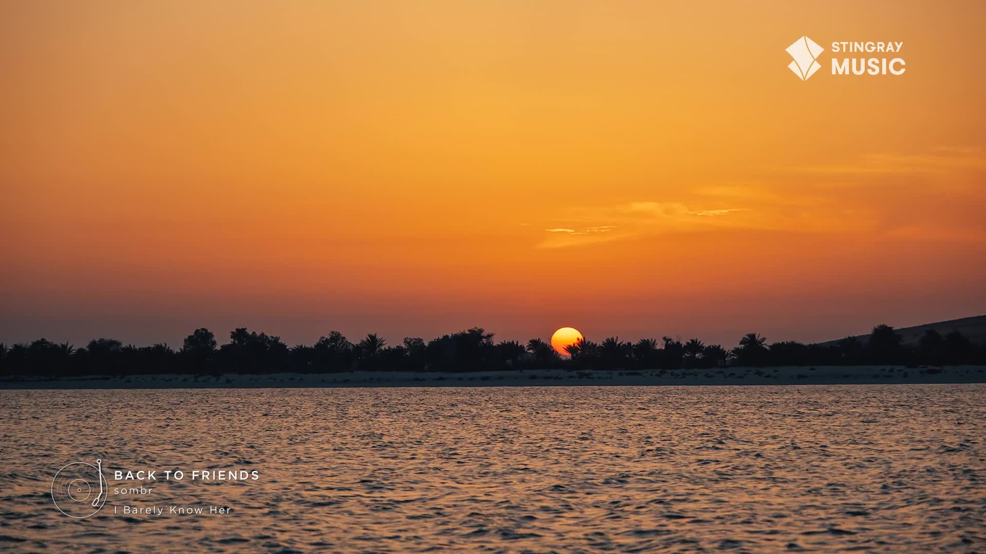 The sun dips below the treeline, painting the sky a fiery orange. Ripples break the surface of the water, reflecting the warm glow of dusk.