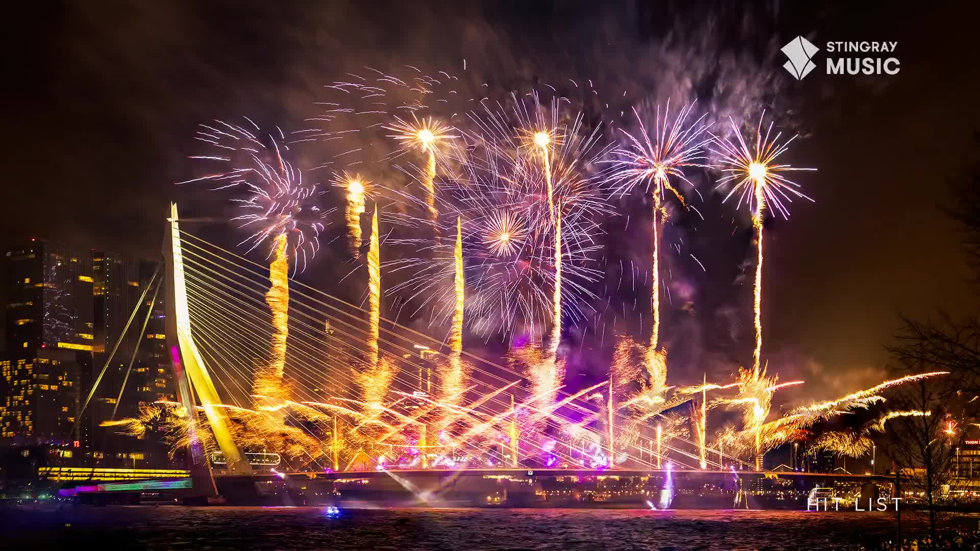 Fireworks burst in vibrant purples and golds over a modern cable-stayed bridge, illuminating the night sky. The Stingray Hit List logo is visible in the corner.
