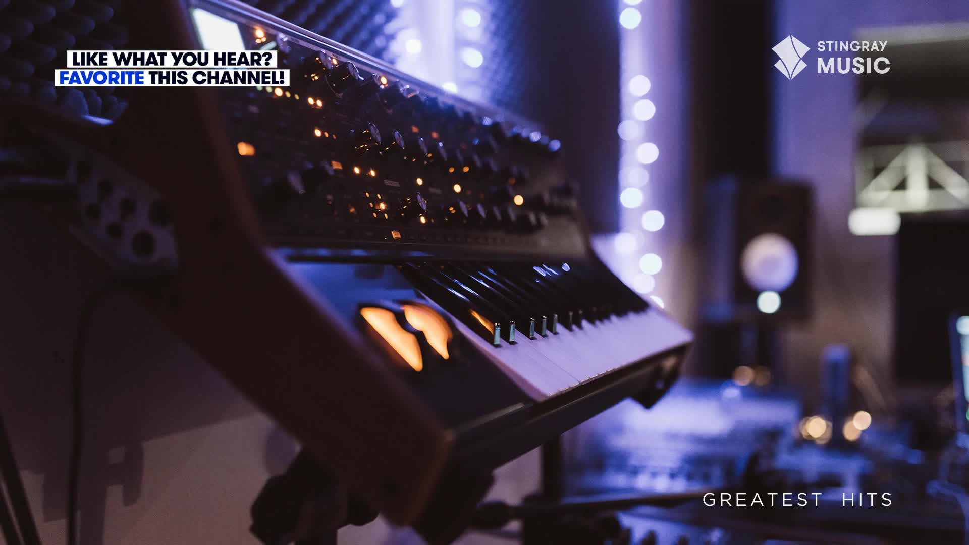 A keyboard's keys are lit up, and the instrument is angled towards me. The scene is bathed in cool tones, likely a recording studio, with the Stingray Music logo and "Greatest Hits" displayed.

