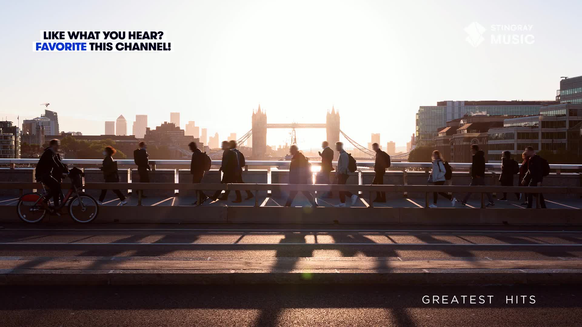 People are walking across a bridge, their silhouettes cast long shadows in the early morning light. A cyclist pedals past, while in the background, the iconic Tower Bridge stands silhouetted against the sunrise.
