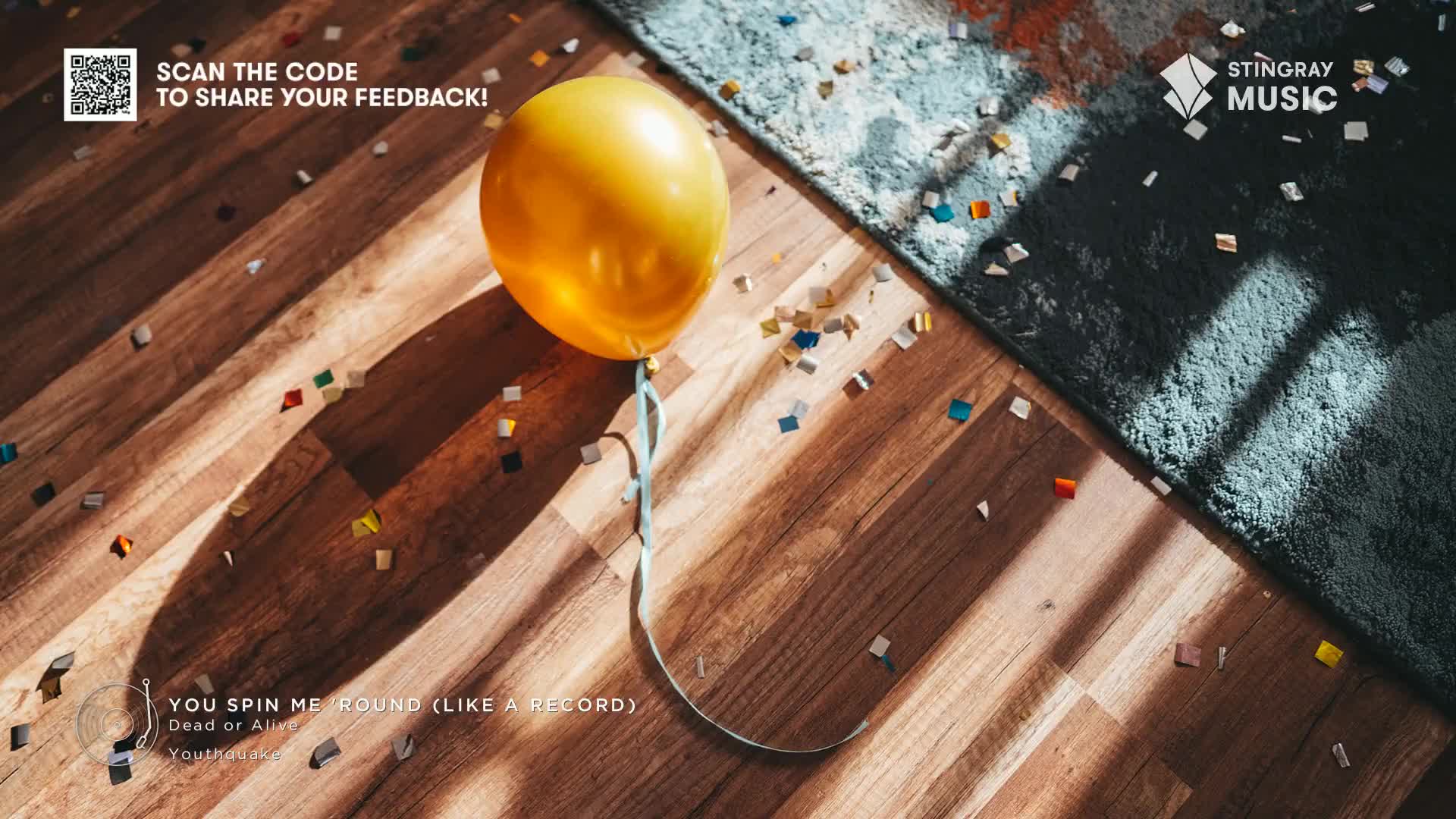 A bright yellow balloon floats above a wooden floor scattered with confetti, a light blue ribbon dangling below. The sunlight casts long shadows across the scene, and a corner of a blue rug adds a contrasting texture.
