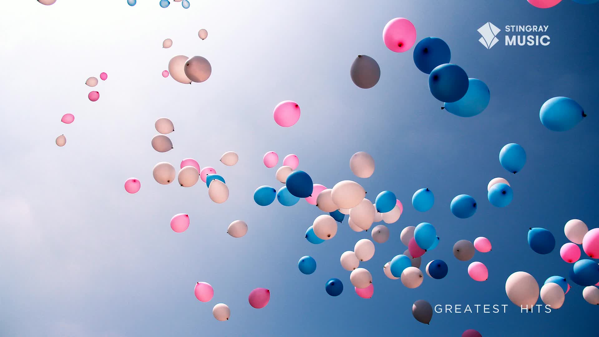 Pink, blue, and white balloons drift upward against a bright blue sky. It looks like a celebration, maybe something to do with the Stingray Holiday Hits broadcast from Canada.
