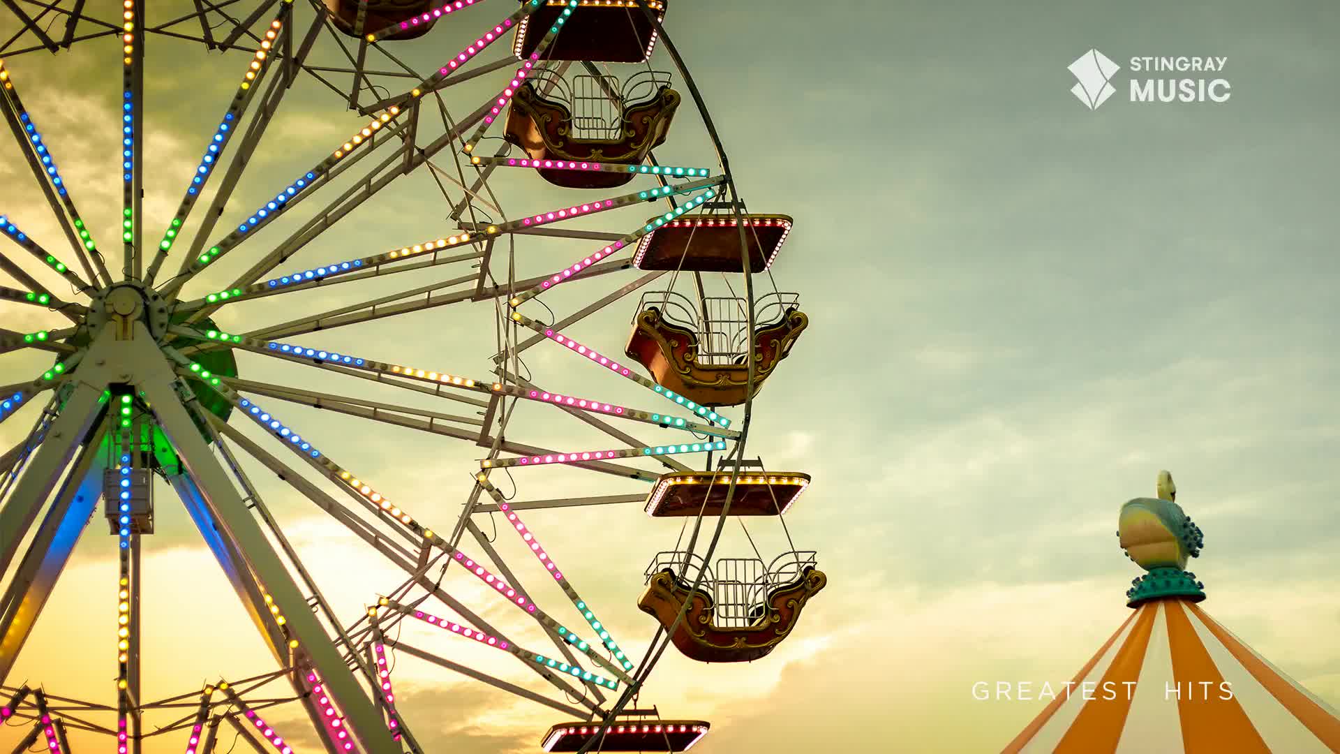 The Ferris wheel's lights are a rainbow against the overcast sky, and the gondolas are empty. The Stingray Music logo, a Canadian staple, is visible as the Ferris wheel sits still at this fair.
