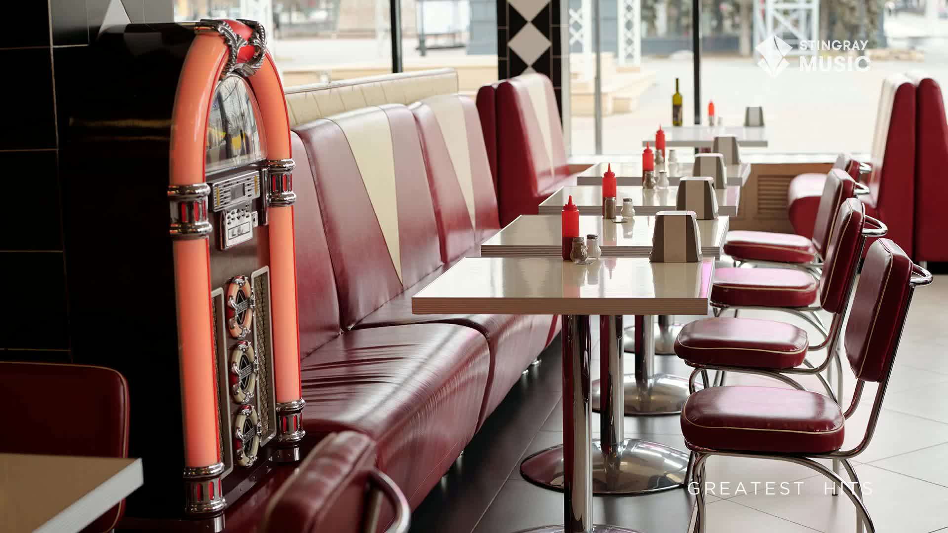 A retro diner, likely somewhere in Canada, is empty, with red vinyl booths and chrome-legged tables.  A jukebox, glowing in a peachy light, stands ready to play some Stingray Holiday Hits.
