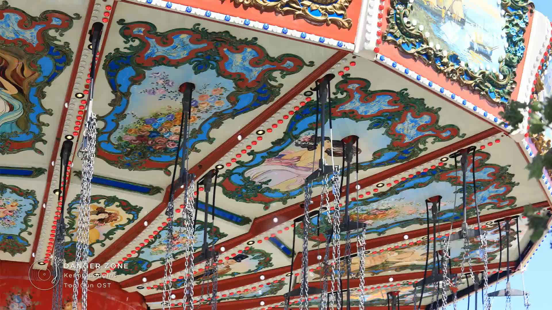 The ornate ceiling of a swing ride spins overhead, its painted panels a riot of color. Chains dangle, ready to lift riders high above the ground, maybe to the tune of Stingray Holiday Hits.
