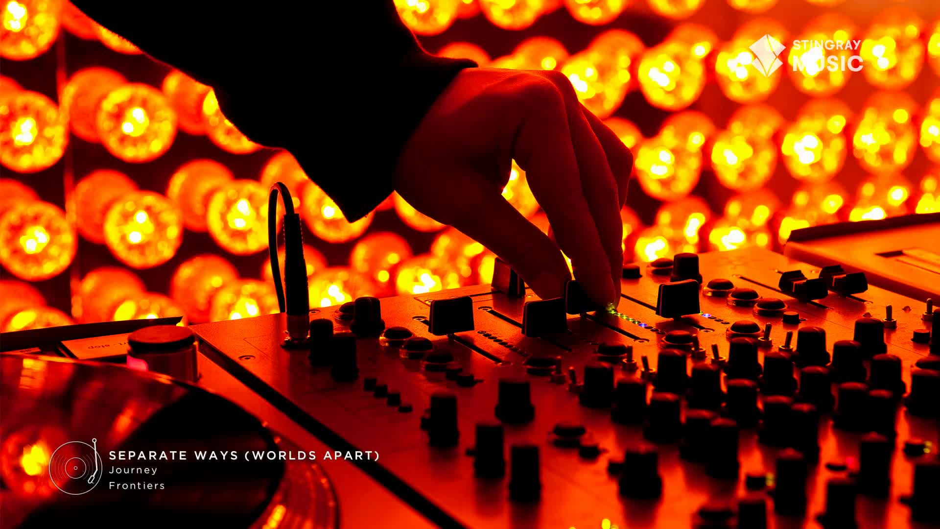 A hand hovers over a mixing board, adjusting the levels as "Separate Ways (Worlds Apart)" by Journey plays. The warm, orange glow of lights behind the equipment creates a vibrant atmosphere, likely for a Stingray Holiday Hits broadcast in Canada.
