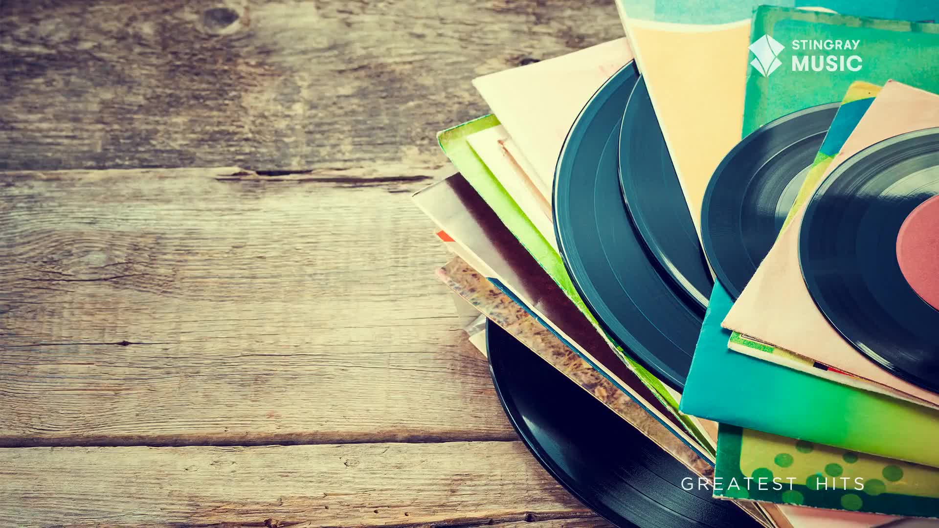 A stack of vinyl records, some with their covers visible, rests on weathered wooden planks. The Stingray Music logo hints at a playlist of holiday hits, perhaps for Canada.
