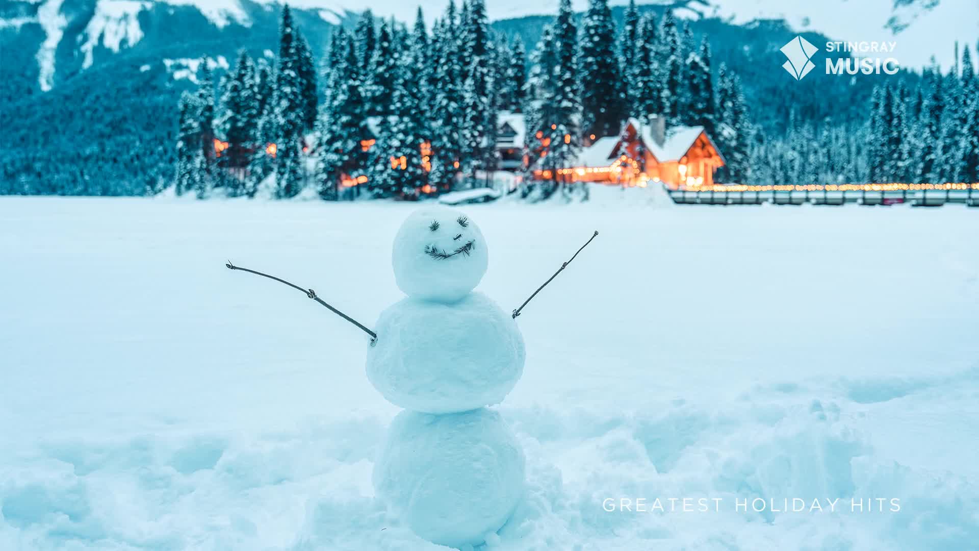 A snowman, arms outstretched, stands on a snow-covered lake, a cheerful face drawn on its head. Behind, a cozy lodge glows with lights, nestled among snow-laden evergreens in the Canadian winter scene.
