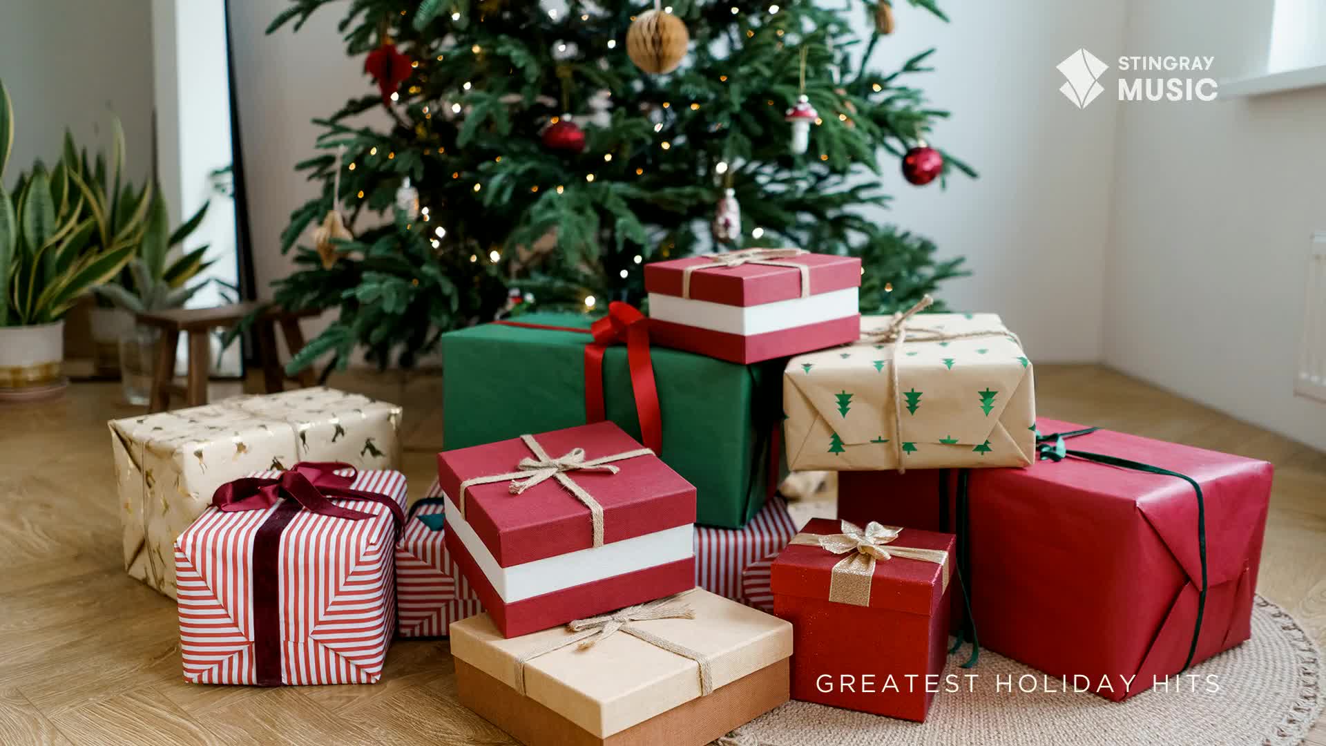 Presents wrapped in festive paper are piled around a Christmas tree, ready for the holidays. The Stingray Holiday Hits logo is visible, promising a soundtrack for the season.
