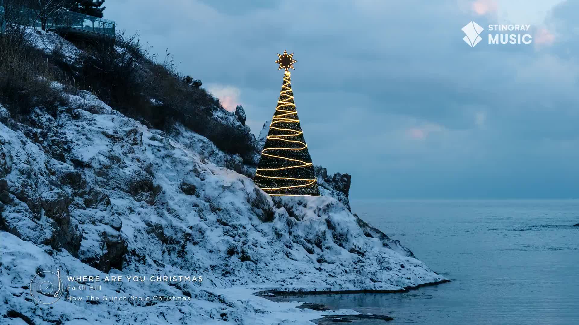 A solitary, illuminated Christmas tree stands proudly on a snowy cliff overlooking the sea, a beacon against the twilight sky. The Stingray Holiday Hits logo and "Where Are You Christmas" text are visible, adding to the Canadian winter scene's festive atmosphere.
A solitary, illuminated Christmas tree stands proudly on a snowy cliff overlooking the sea, a beacon against the twilight sky. The Stingray Holiday Hits logo and "Where Are You Christmas" text are visible, adding to the Canadian winter scene's festive atmosphere.