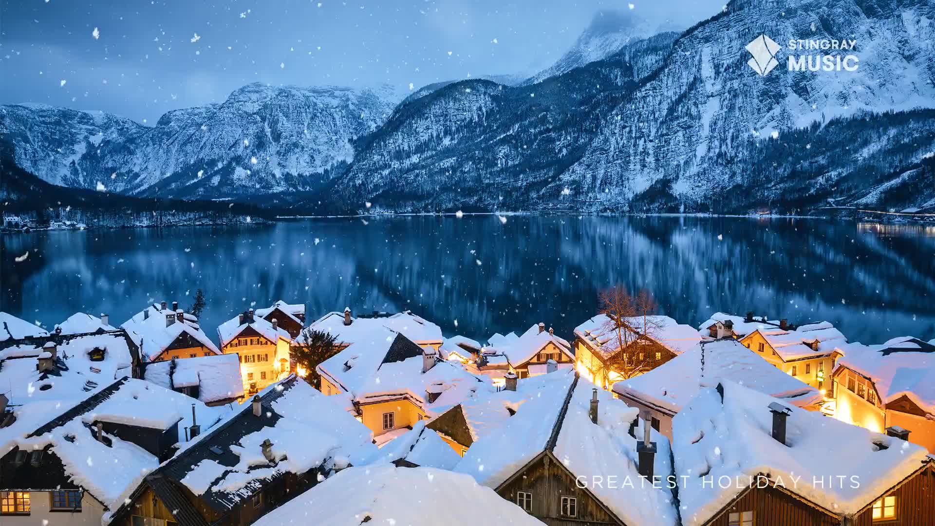 Snowflakes drift down over a village nestled on a lake, the lights in the windows casting a warm glow. The scene feels like a holiday card, maybe something from Stingray Music in Canada.
