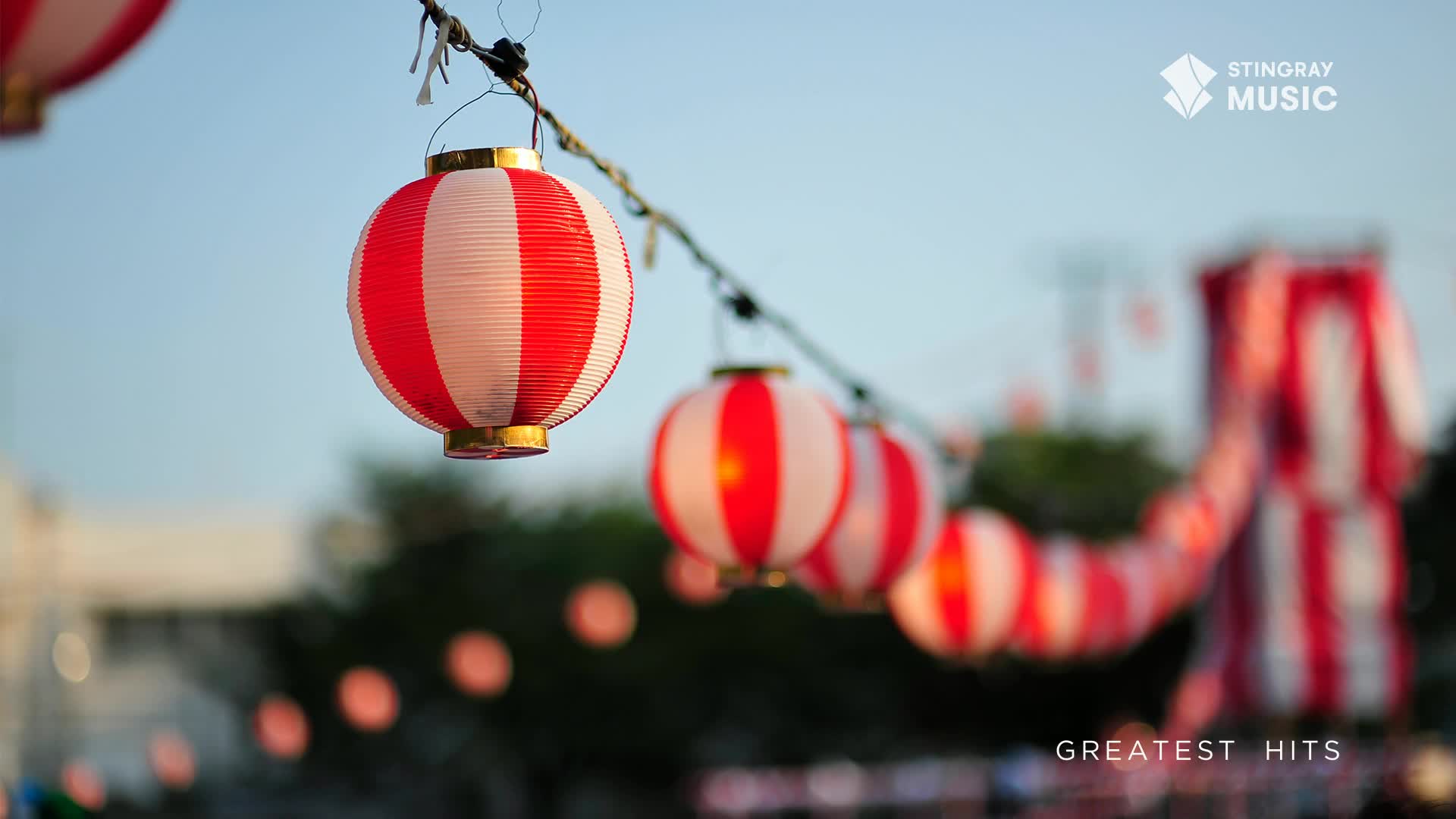 A string of red and white striped lanterns hangs across the sky, their gentle glow hinting at a festive evening. In the distance, a large, striped structure, possibly a tent or stage, stands out against the fading light.