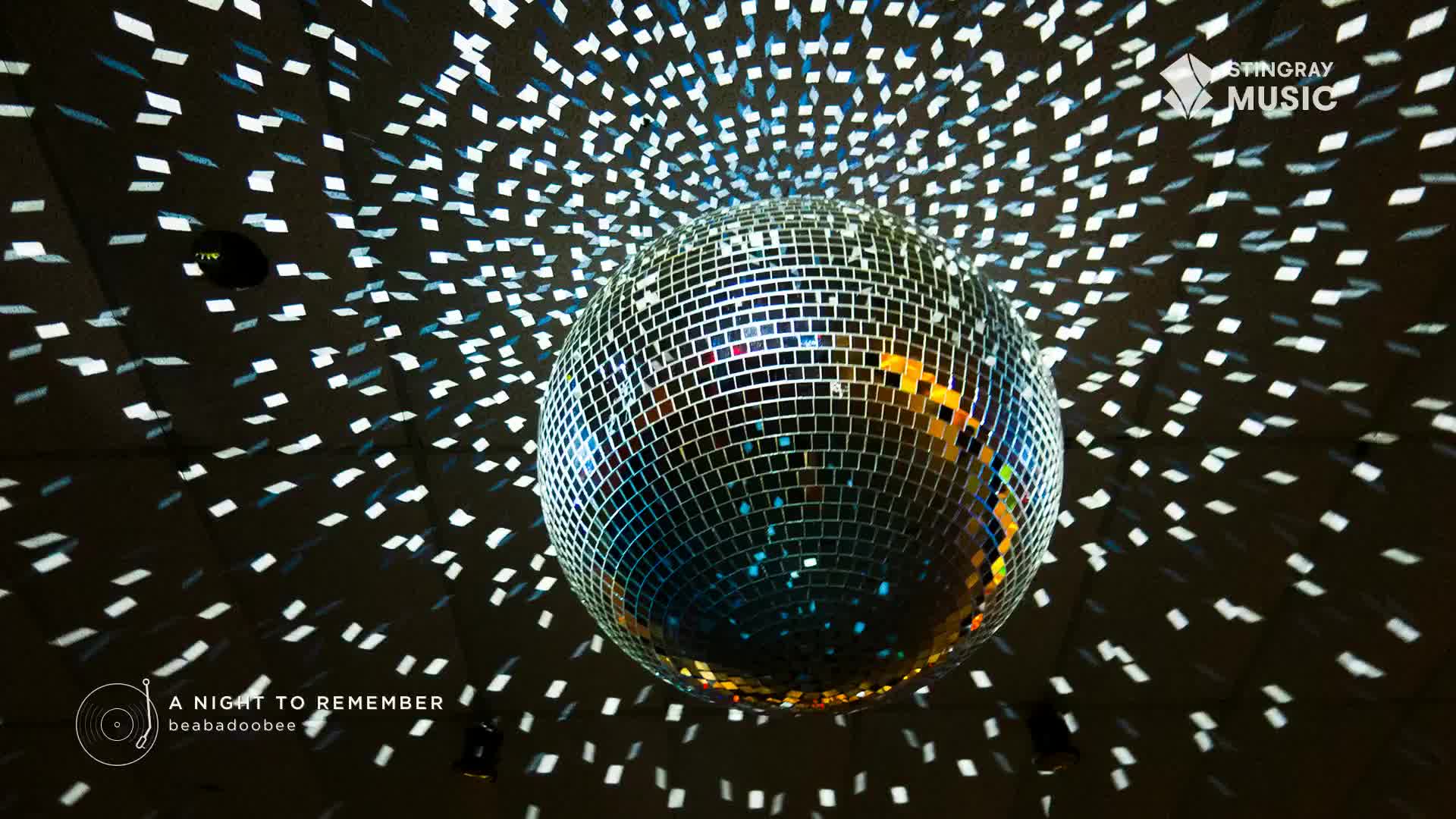 A large disco ball spins, casting a dazzling array of white and blue light patterns across the dark ceiling. This is the scene at a Stingray Holiday Hits event in Canada.