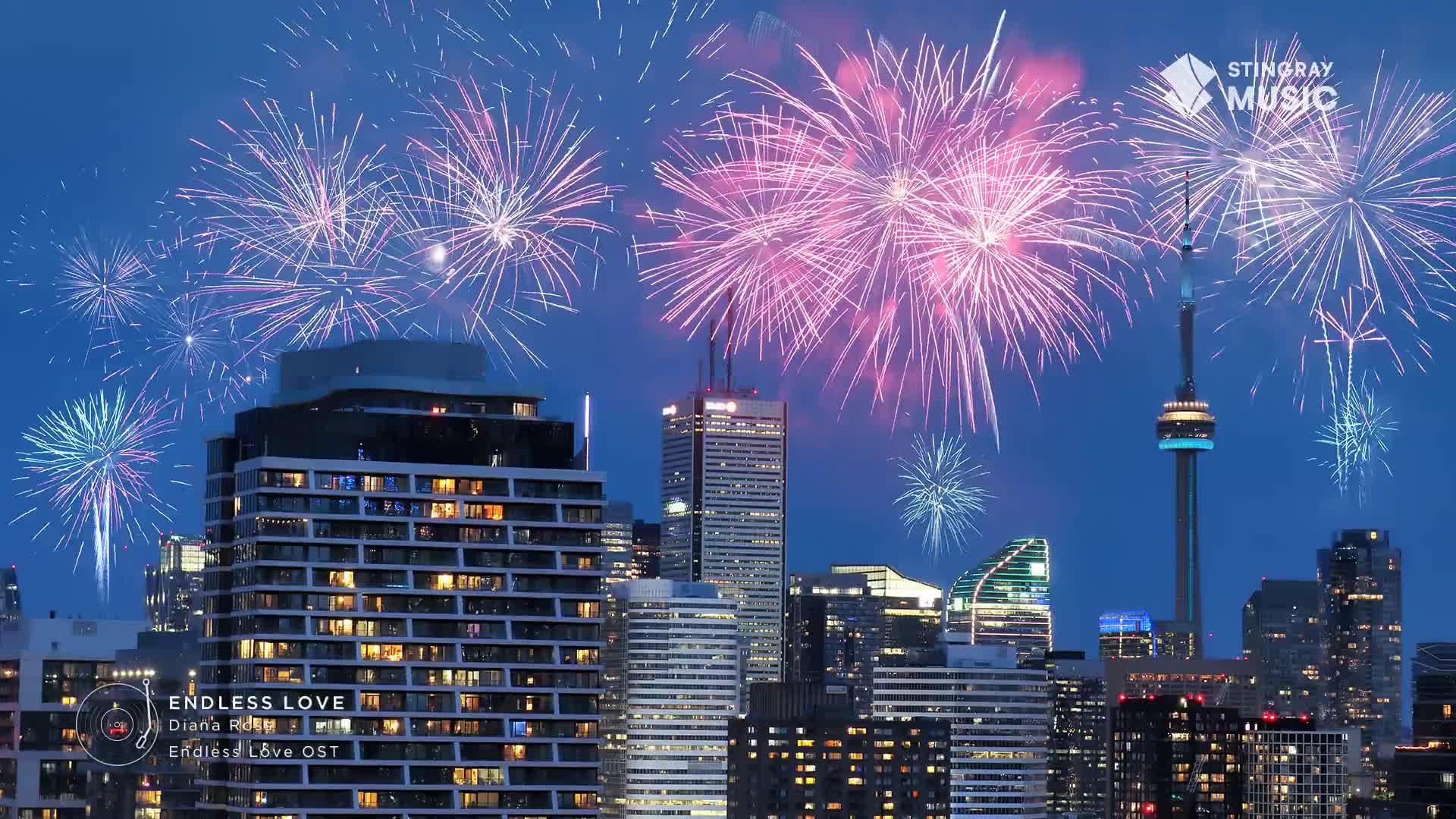 Pink and white fireworks explode above Toronto's skyline, illuminating the CN Tower and surrounding buildings.  The Stingray Music logo is visible in the upper right corner, and a graphic for "Endless Love" plays on a screen.