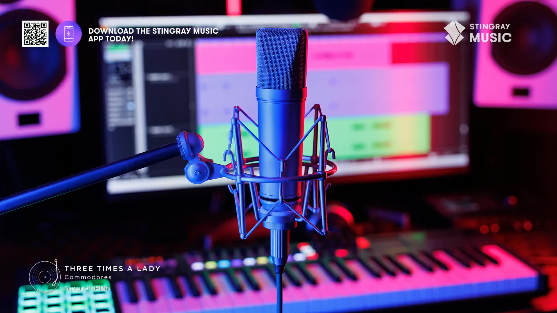 A blue condenser microphone stands ready in front of a computer screen displaying audio editing software. The keyboard of a synthesizer glows with pink and blue light beneath the microphone.