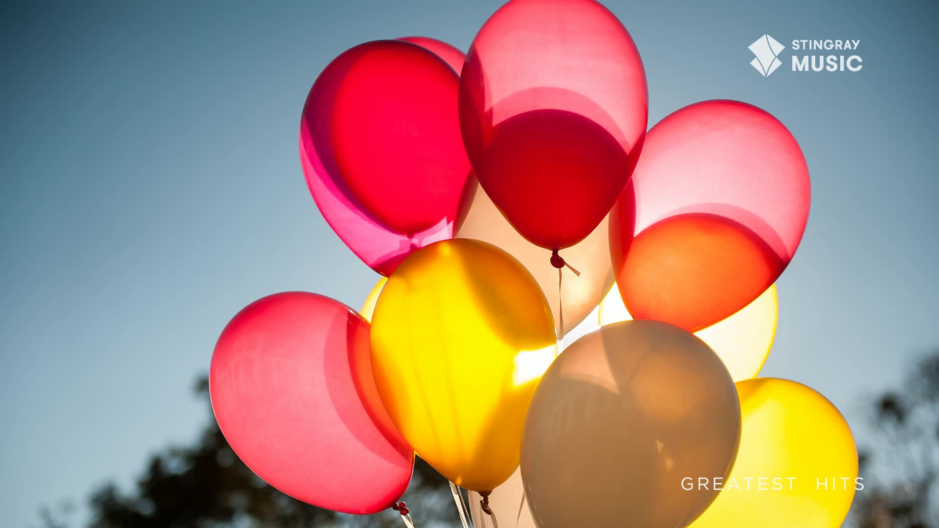 A cluster of bright balloons bobs against the clear sky, their colours a cheerful mix of red, yellow, and pink. The Stingray Music logo sits in the upper right corner, hinting at a festive holiday playlist.