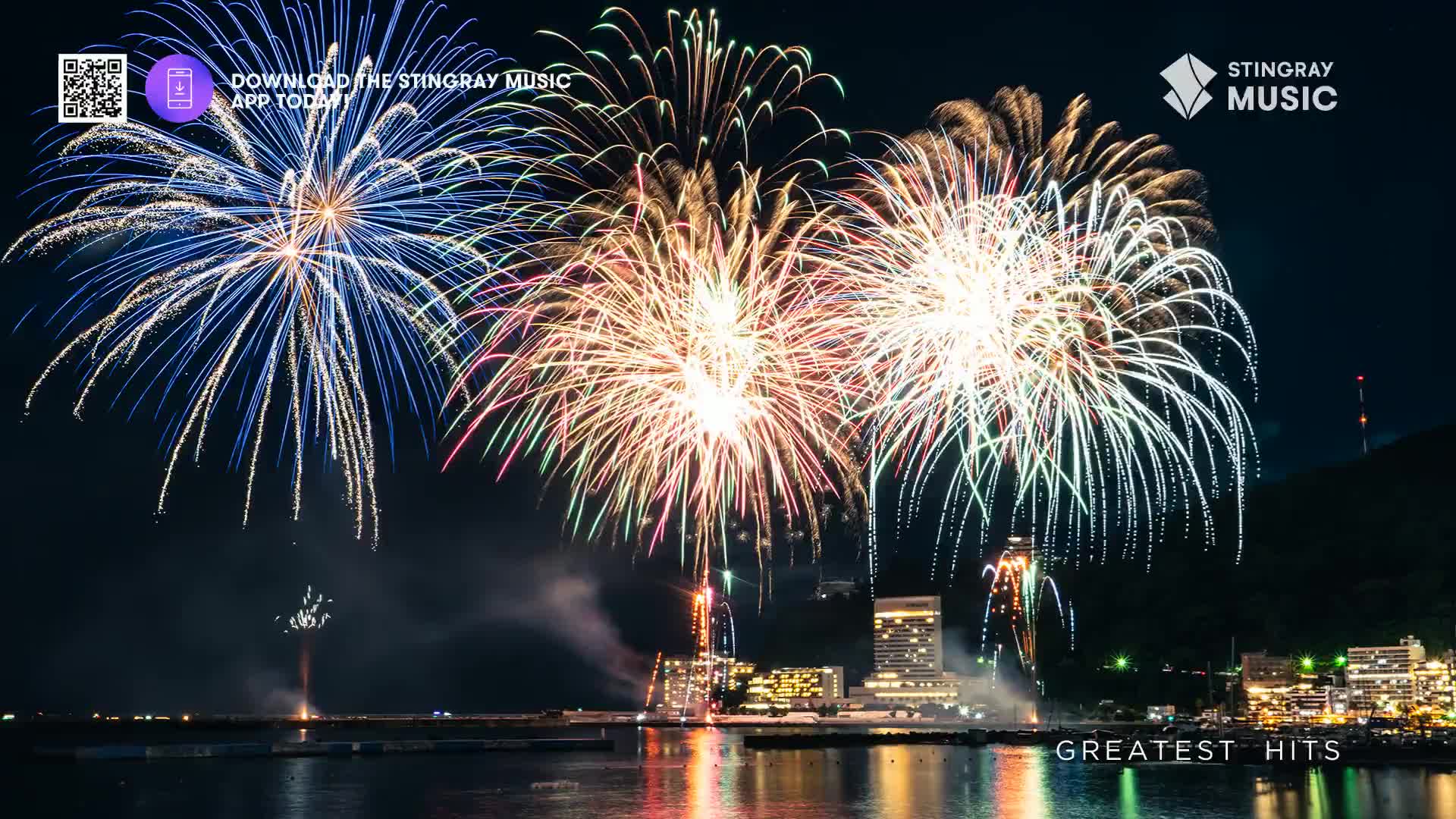 Explosions of light bloom across the dark sky, reflecting on the water below. Buildings glow along the shore, a vibrant backdrop to this Canadian holiday celebration.