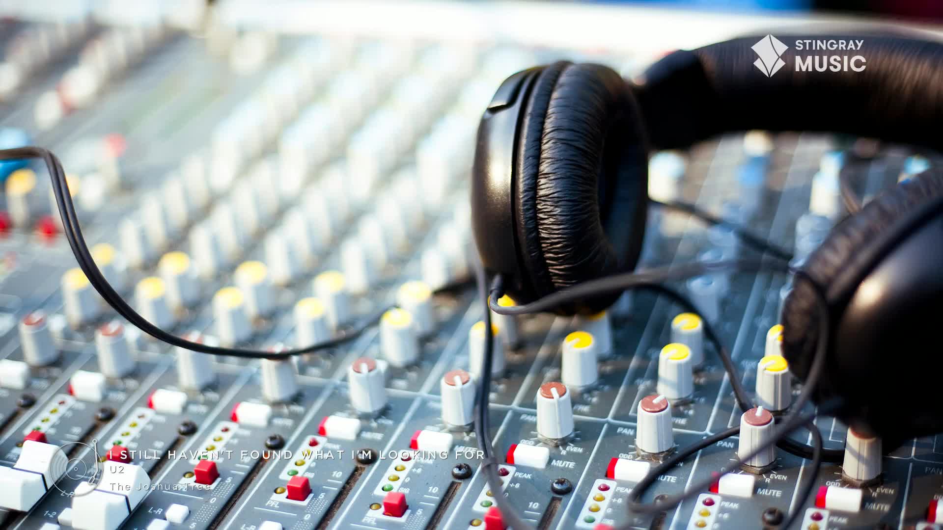 Headphones rest on a soundboard, ready for the next track from Stingray Holiday Hits. The faders are set, and a black cable snakes across the controls.