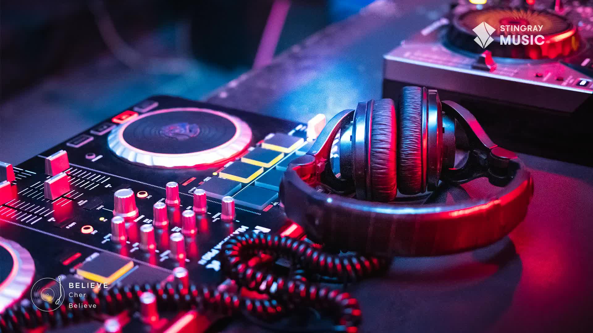 A DJ console glows with red and blue lights, ready for a set. Headphones rest on their stand, their coiled cord a dark tangle.