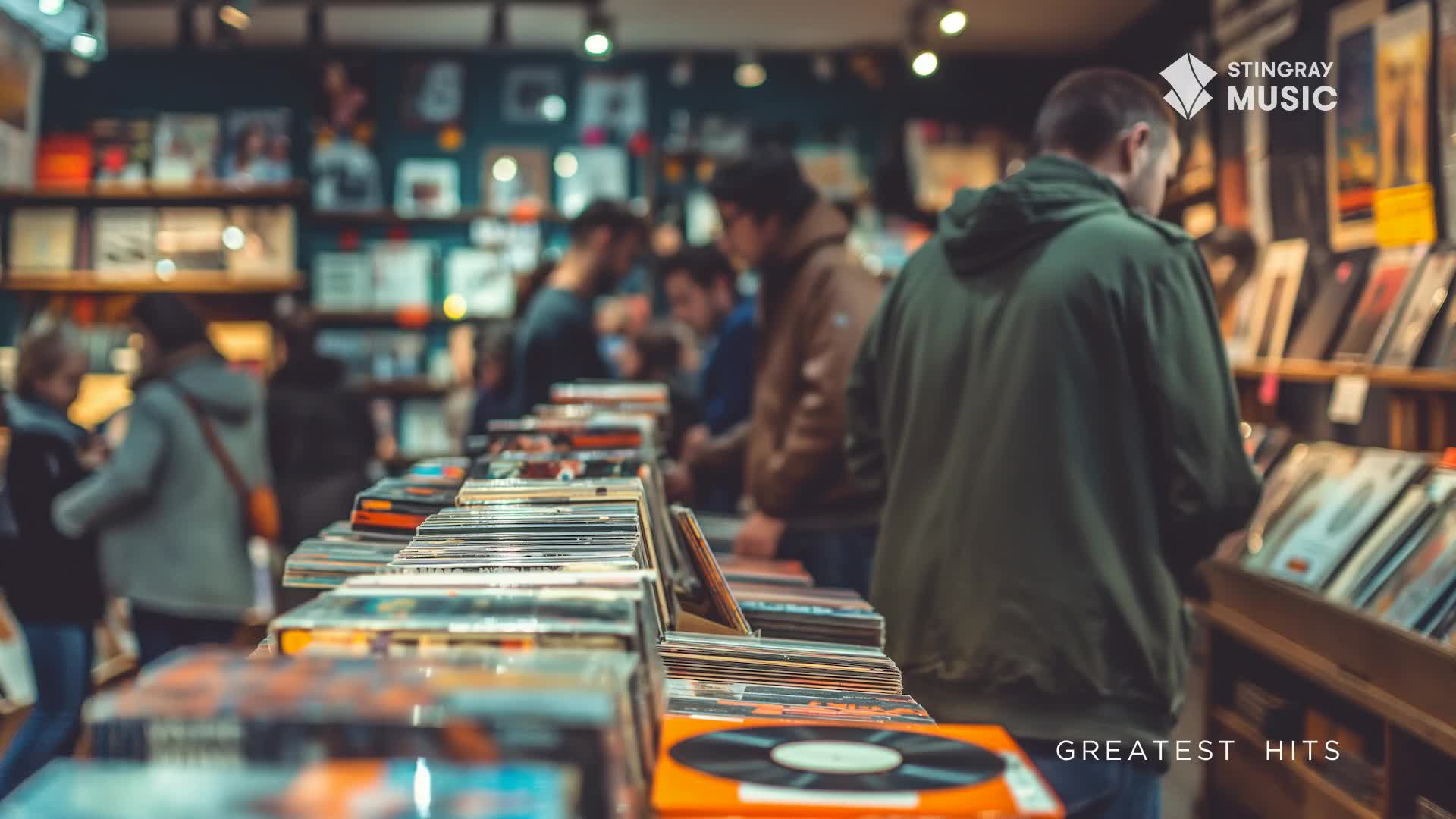 People browse through stacks of records in a dimly lit shop. A man in a green hoodie stands by a shelf, looking at the vinyl.