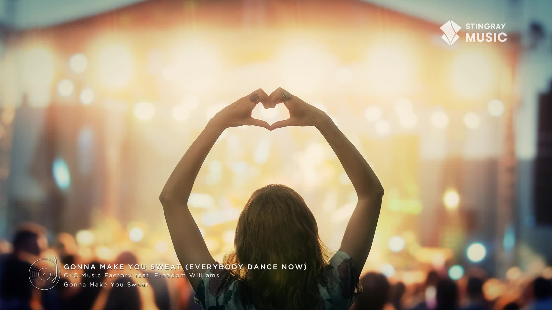 The stage lights glow warmly on the crowd as a fan holds their hands up, forming a heart shape. This is a Stingray Holiday Hits event, and the energy is electric.