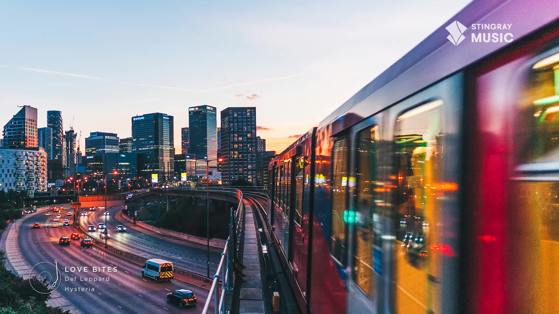 A red train speeds past, its windows reflecting the city lights as the sun sets over the Canadian skyline. Below, cars navigate a highway, their headlights creating streaks of light.
