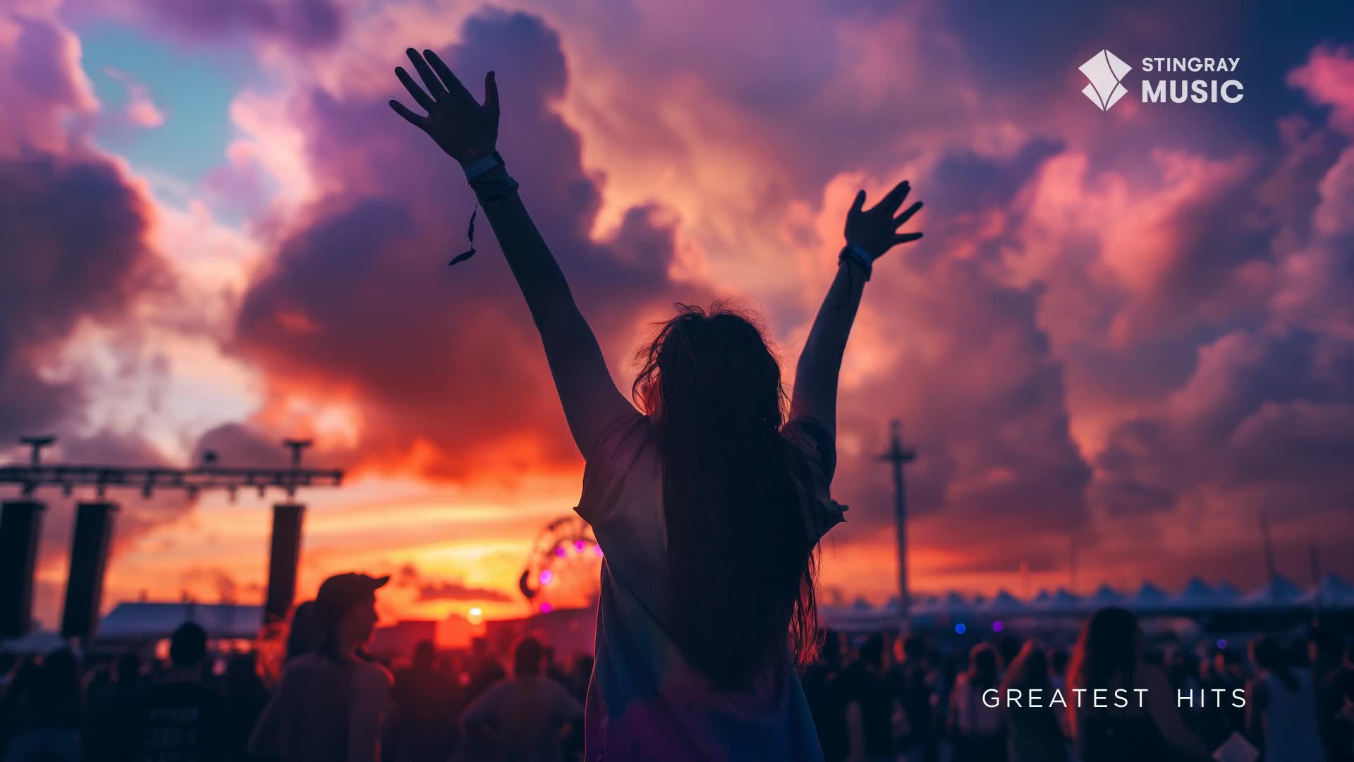 The sky bleeds orange and purple as a crowd gathers for a concert in Canada. A person in the foreground throws their arms up, celebrating the music.