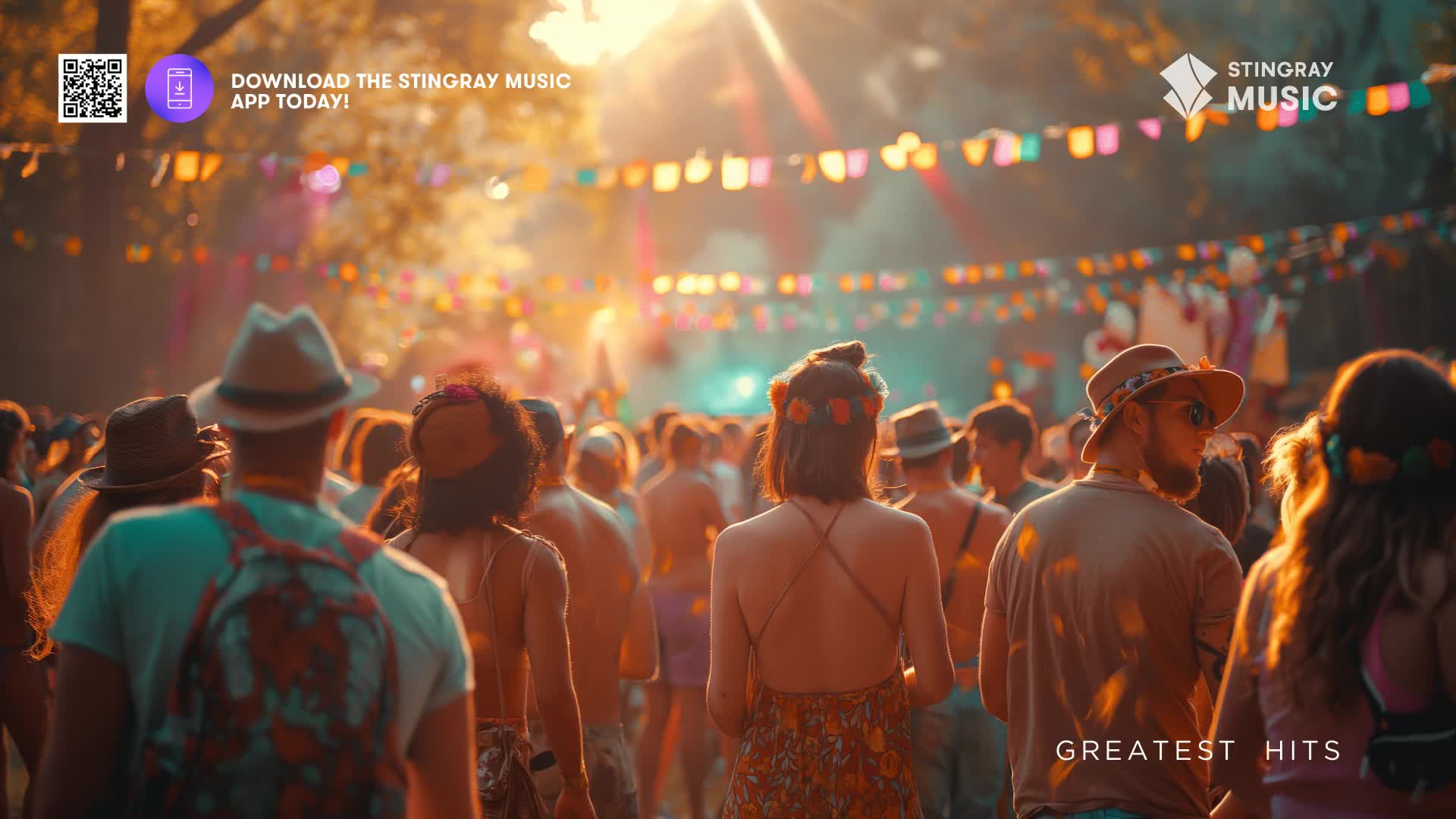 A crowd mills about under a canopy of colorful flags, the late afternoon sun casting long shadows. People are dressed in casual summer attire, some with flowers in their hair, suggesting a festival atmosphere.
