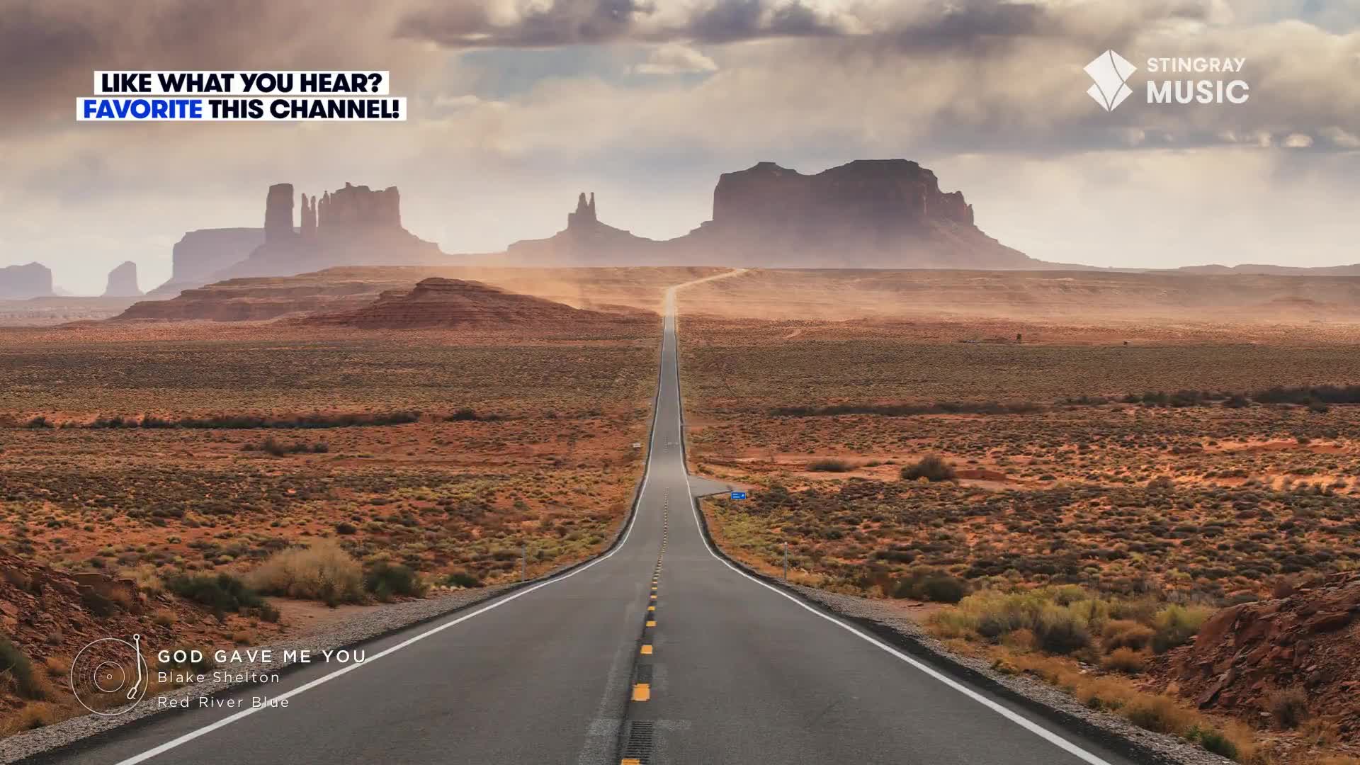 A long, straight road stretches into the distance, disappearing towards the hazy buttes. The Stingray Music logo sits in the corner, and the song "God Gave Me You" by Blake Shelton plays on Hot Country.
