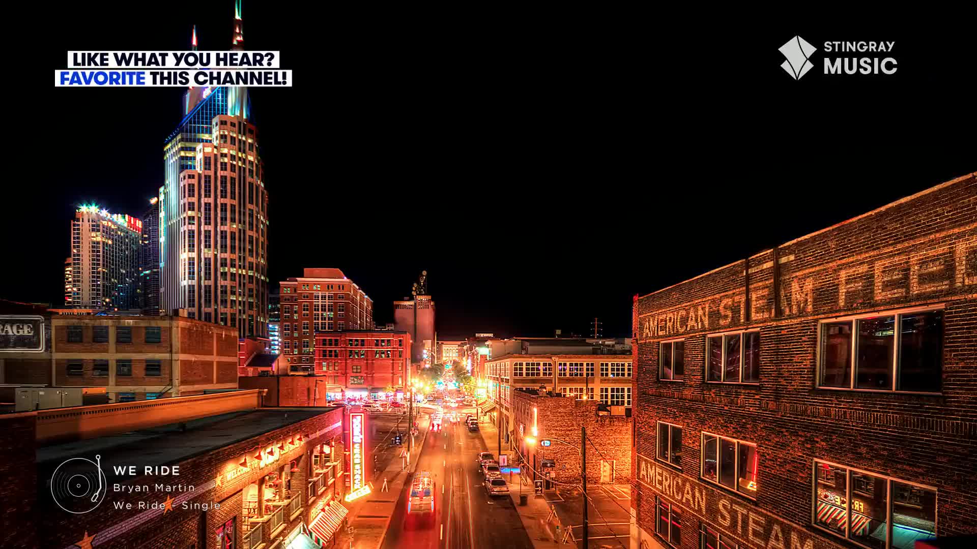 Neon signs glow on a brick building, while traffic moves slowly down a street lined with buildings. The Stingray Music logo is in the corner, and the song "We Ride" by Bryan Martin is playing.
