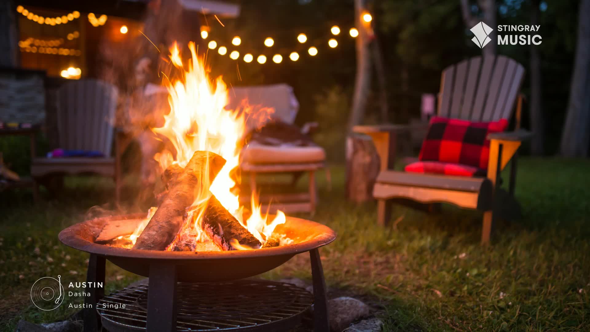 Flames dance upwards from the logs in the fire pit, casting a warm glow over the Adirondack chairs and a red and black plaid pillow. Overhead, a string of lights twinkles, setting the mood for a perfect Canadian evening.
