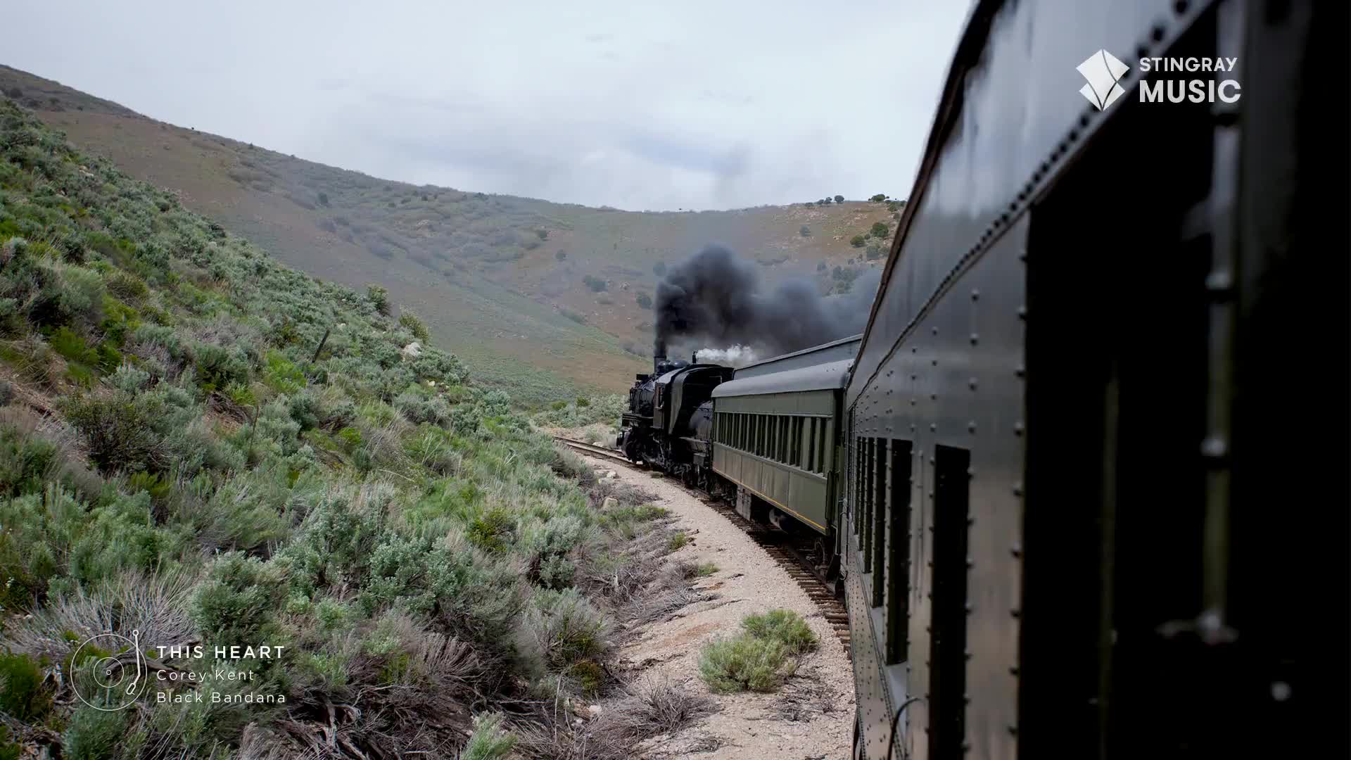 The train, belching black smoke, curves along the tracks through the hills. The side of the car I'm standing next to is a dark, reflective green.
