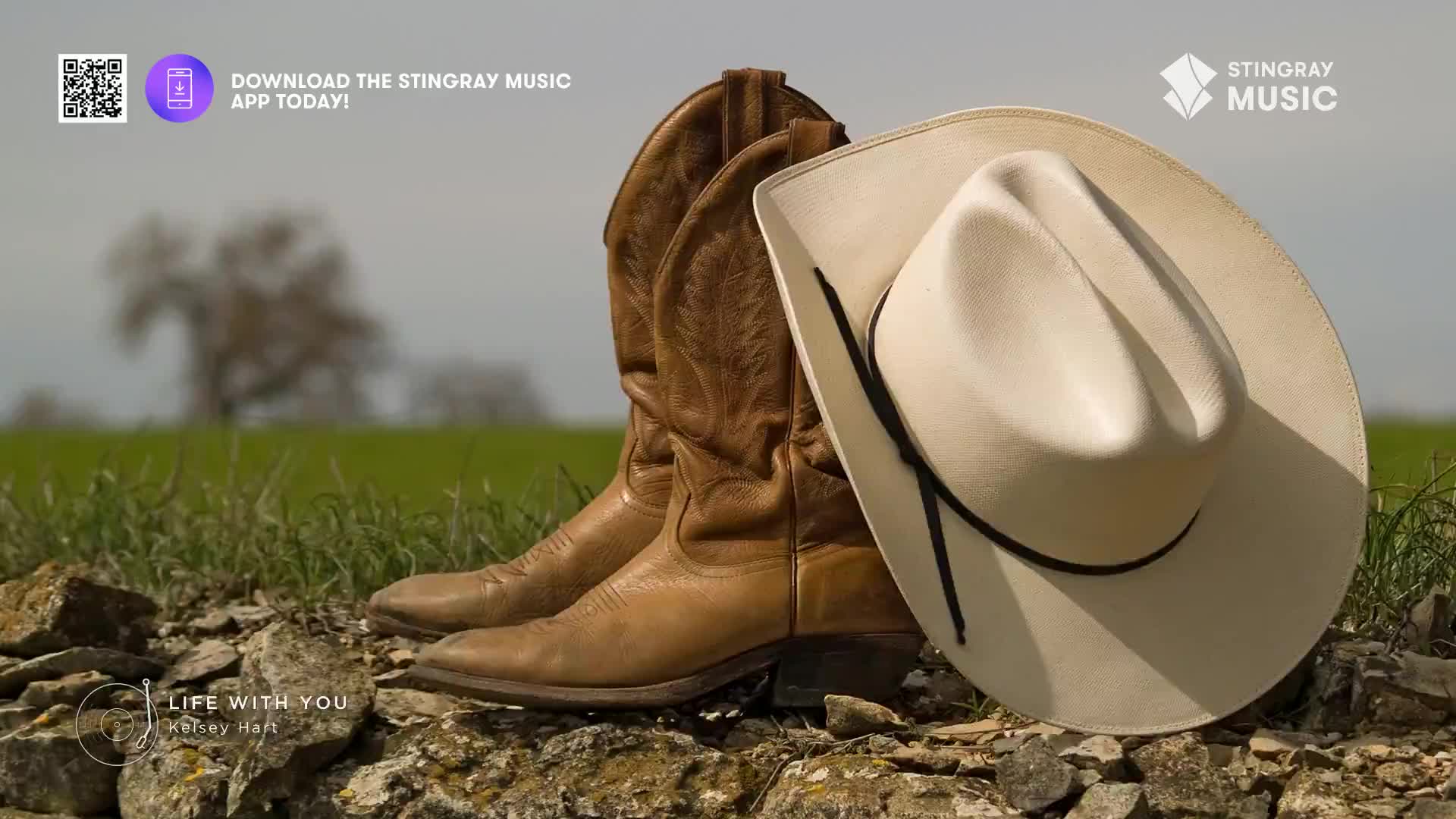 A pair of well-worn cowboy boots and a white hat rest on a stone wall, the backdrop a green field and a hazy sky. The Stingray Music logo and a call to download the app are in the corner, suggesting a connection to country music.
