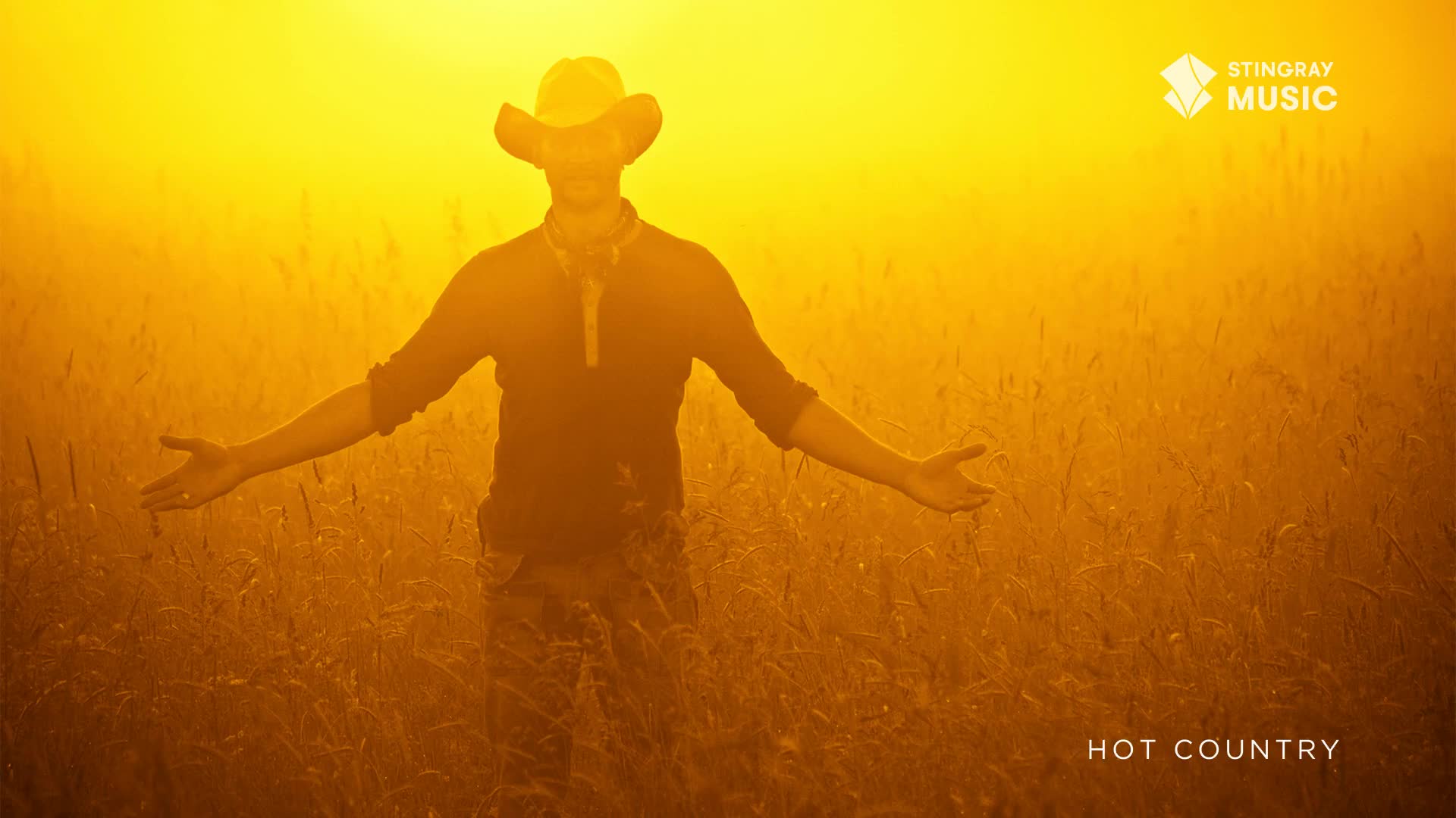 A man in a cowboy hat stands in a field, arms outstretched, bathed in golden light. The Stingray Hot Country logo is in the corner, and the scene feels like a warm, Canadian summer day.
