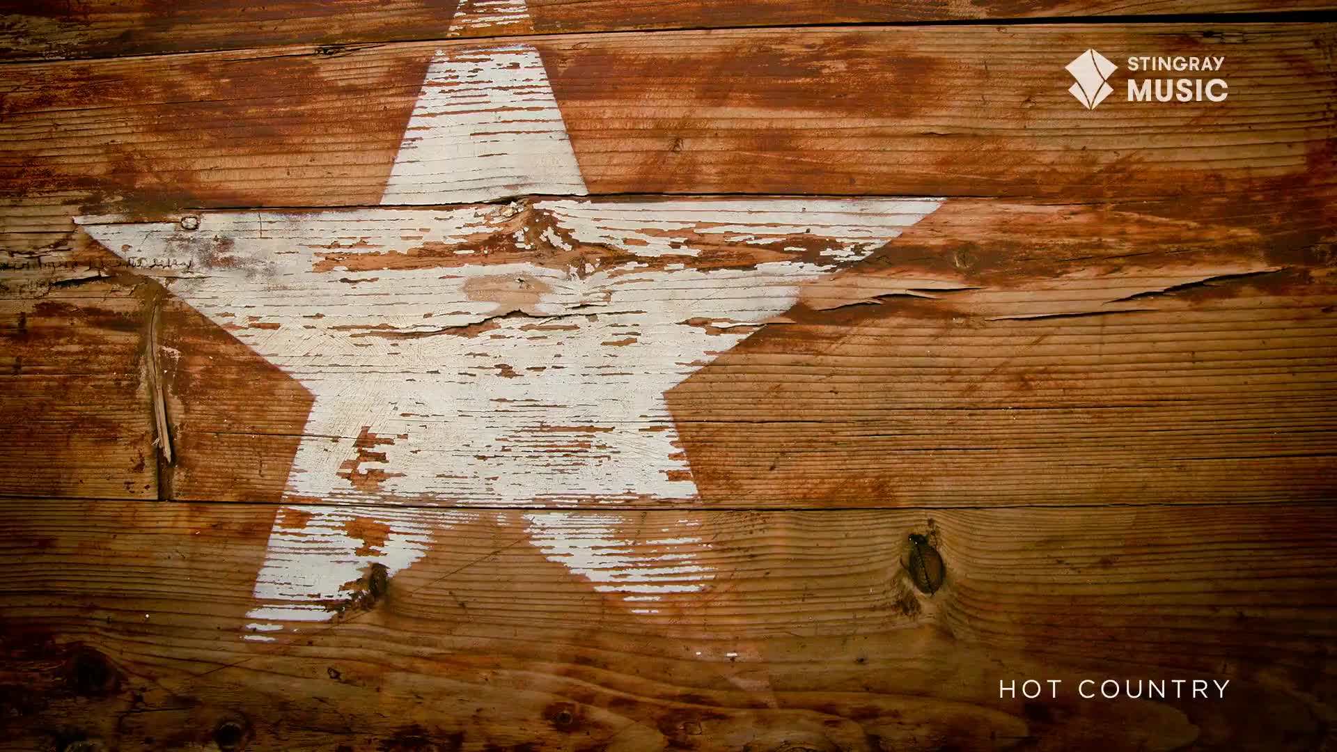 A white, chipped star is painted on weathered wooden planks. The Stingray Hot Country logo sits in the top right corner, with "Hot Country" at the bottom.
