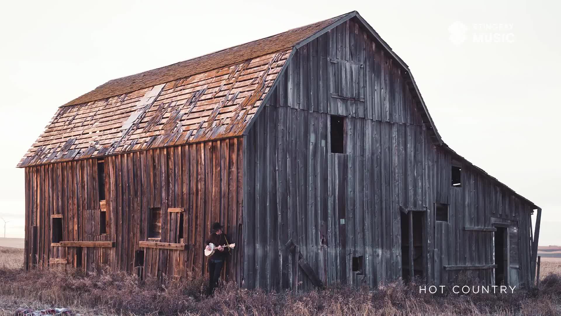 A musician, guitar in hand, leans against the weathered wood of a barn. The old structure, a backdrop for Stingray Hot Country, stands stark against the prairie sky.
A musician, guitar in hand, leans against the weathered wood of a barn. The old structure, a backdrop for Stingray Hot Country, stands stark against the prairie sky.