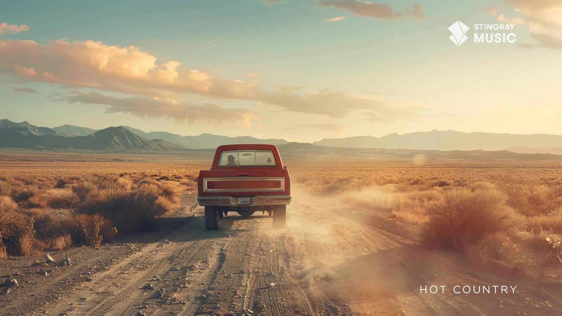 A red pickup truck kicks up dust as it drives down a gravel road through a dry, Canadian landscape. The sun hangs low in the sky, casting long shadows over the sparse brush and distant mountains. A red pickup truck kicks up dust as it drives down a gravel road through a dry, Canadian landscape. The sun hangs low in the sky, casting long shadows over the sparse brush and distant mountains.