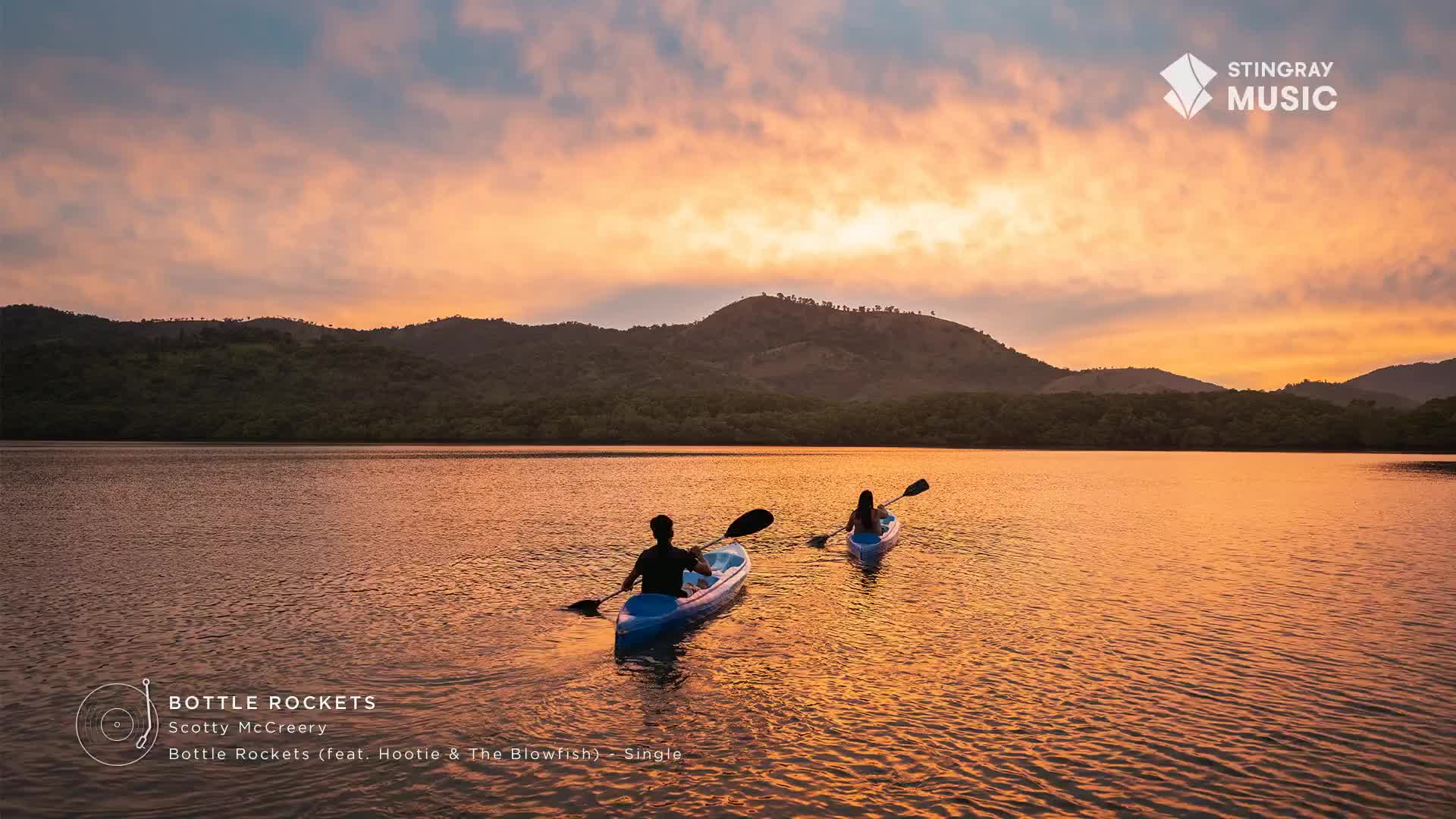 Two kayaks glide across the water, paddles dipping rhythmically. The sky above glows with the warm hues of sunset, reflecting on the calm surface.