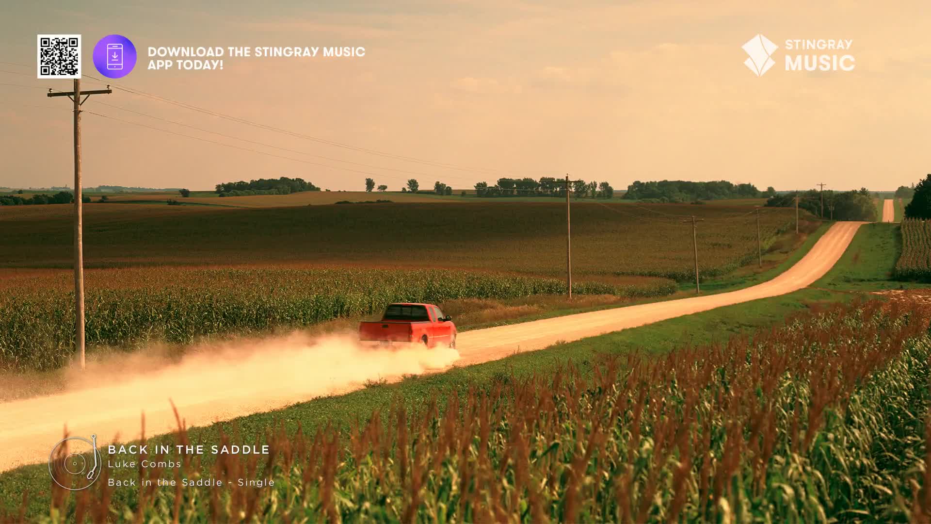 A red pickup kicks up a trail of dust as it speeds down a gravel road through cornfields. The late afternoon sun casts a warm glow over the rolling Canadian landscape.