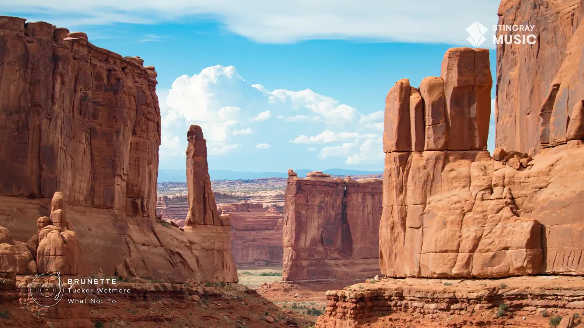 Towering sandstone formations rise from the arid landscape under a bright blue sky. The vast, open space feels like it could be anywhere in the Canadian West, a fitting backdrop for the raw sound of country music.