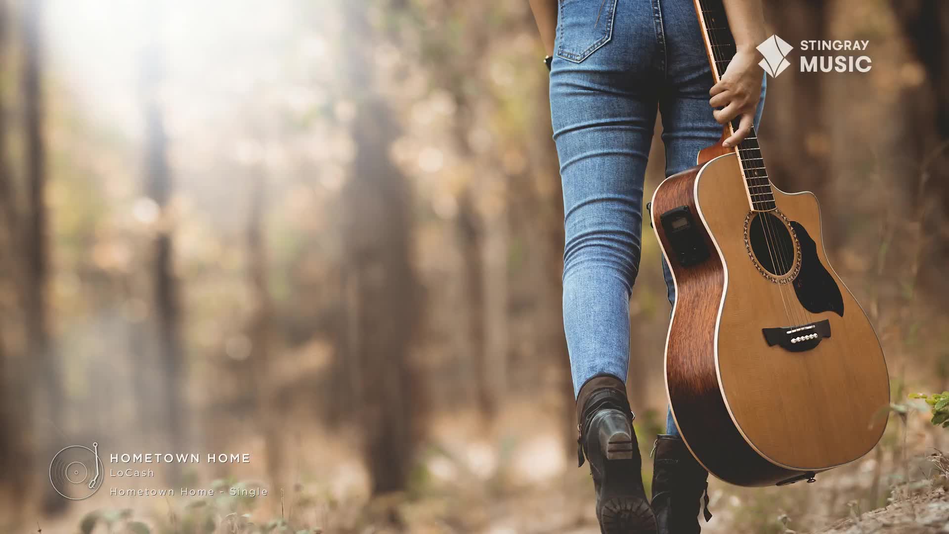 Sunlight filters through the trees as someone in denim jeans and boots walks away, carrying an acoustic guitar. This feels like a quiet moment before a performance, perhaps for Stingray Hot Country.