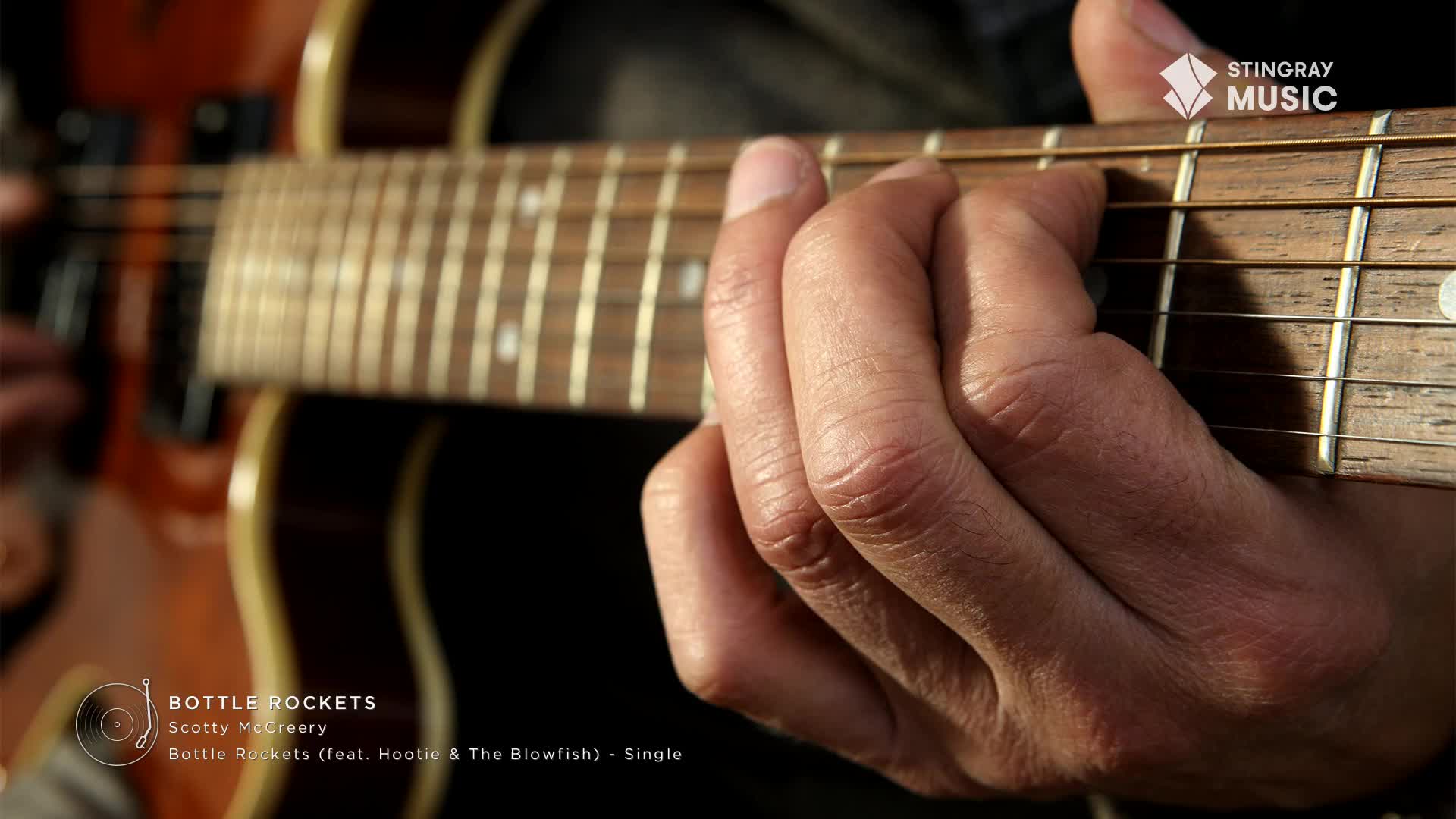 Fingers press down on the fretboard of an electric guitar, the strings vibrating with a country tune. The Stingray Hot Country logo appears in the corner, hinting at a Canadian connection.