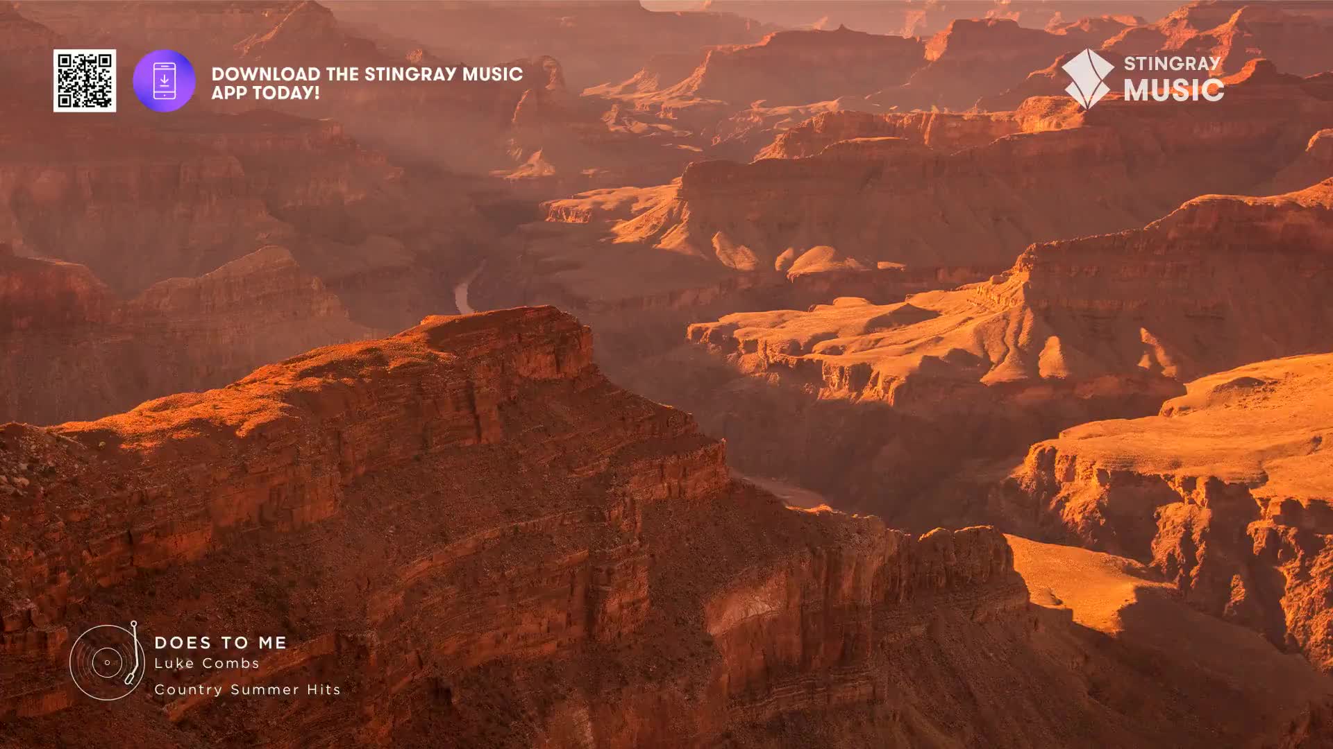 The sun casts long shadows across the vast canyon walls, illuminating the layered rock in shades of orange and brown. A winding river snakes through the landscape far below.