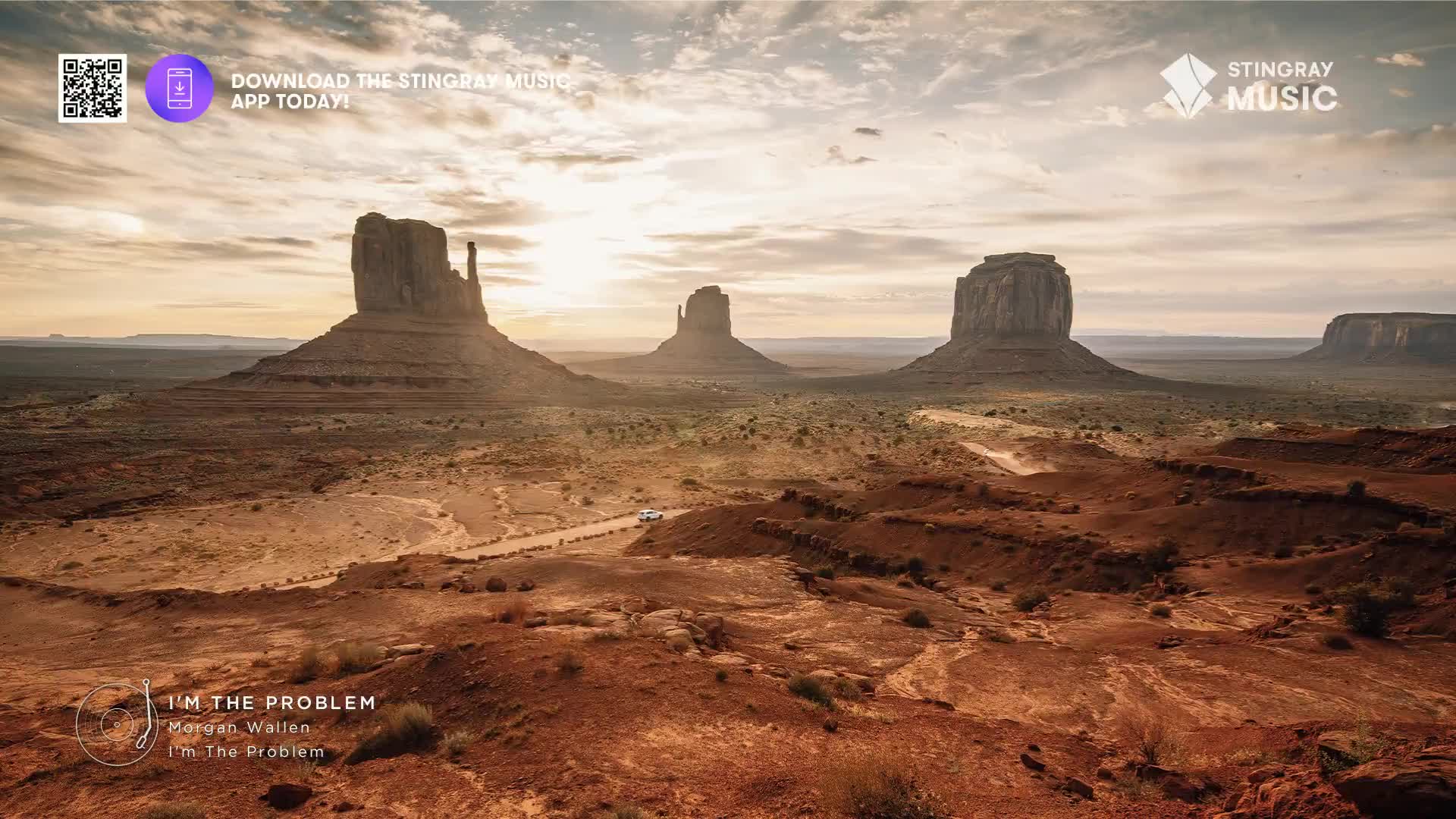 A white vehicle kicks up dust on a dirt road winding through Monument Valley. The sun casts long shadows across the iconic sandstone buttes.