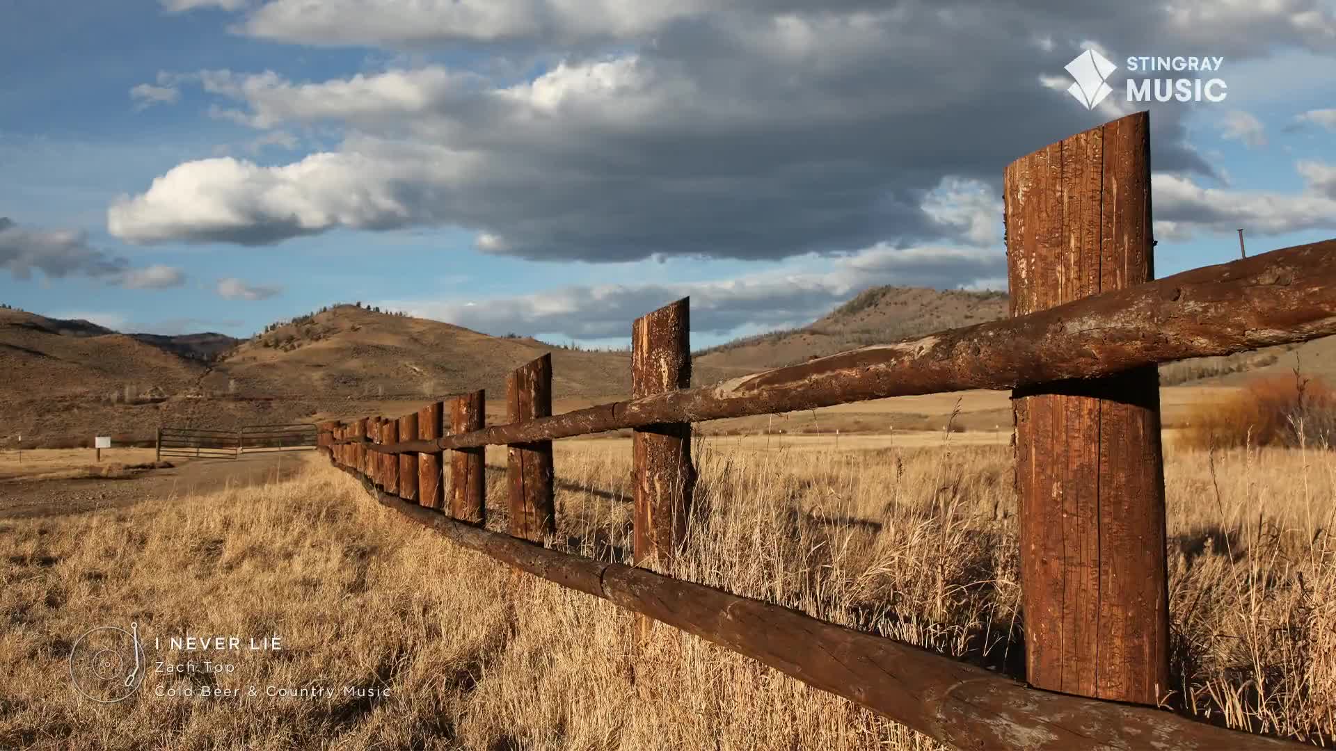 The rough-hewn wooden fence stretches across a dry, golden field under a vast Canadian sky. Hills roll in the distance, their slopes dotted with sparse trees. The rough-hewn wooden fence stretches across a dry, golden field under a vast Canadian sky. Hills roll in the distance, their slopes dotted with sparse trees.