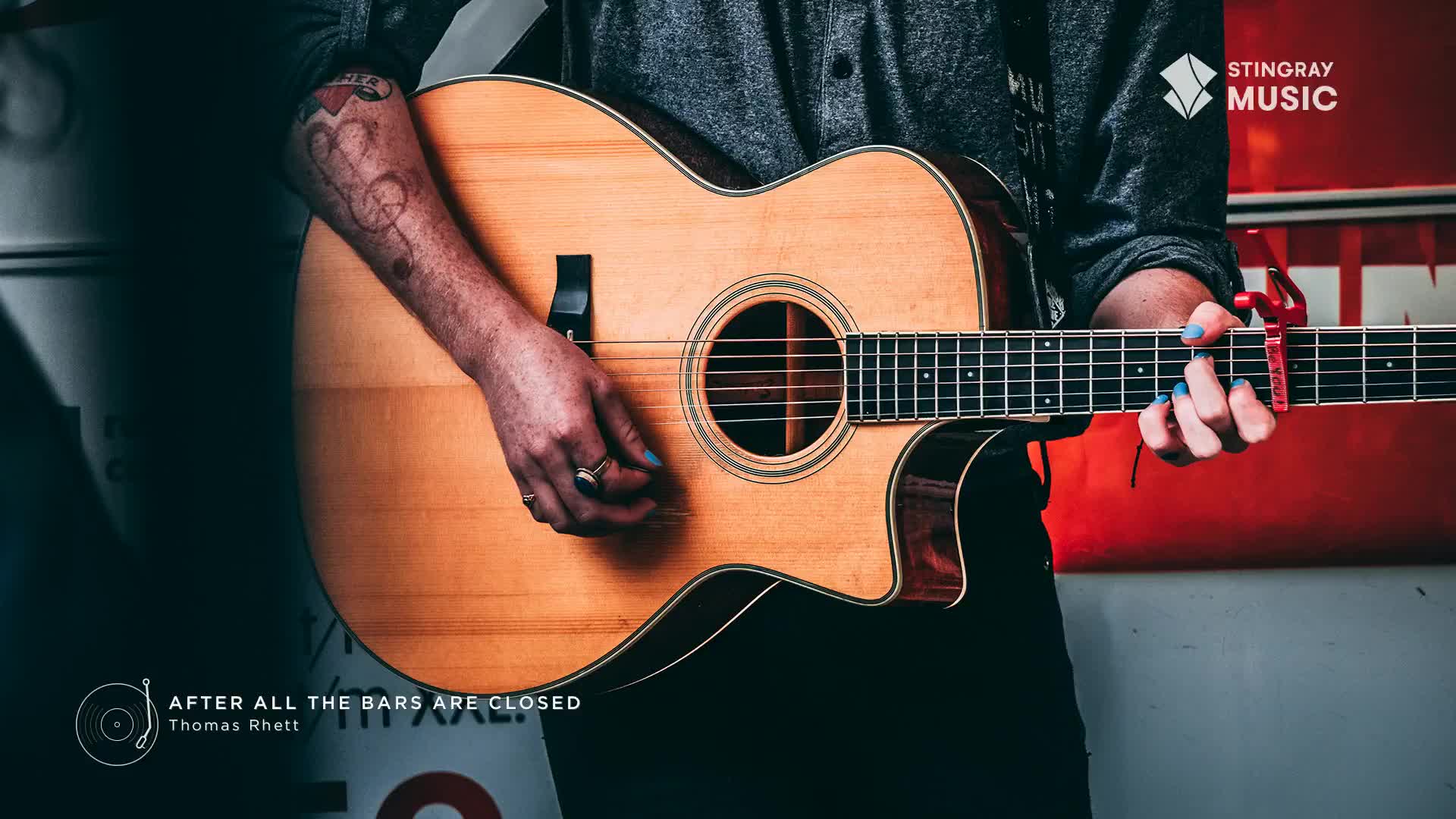 A musician's hands strum a warm-toned acoustic guitar, the red capo a bright accent against the fretboard. The Stingray Hot Country logo appears in the upper right, hinting at the music playing.