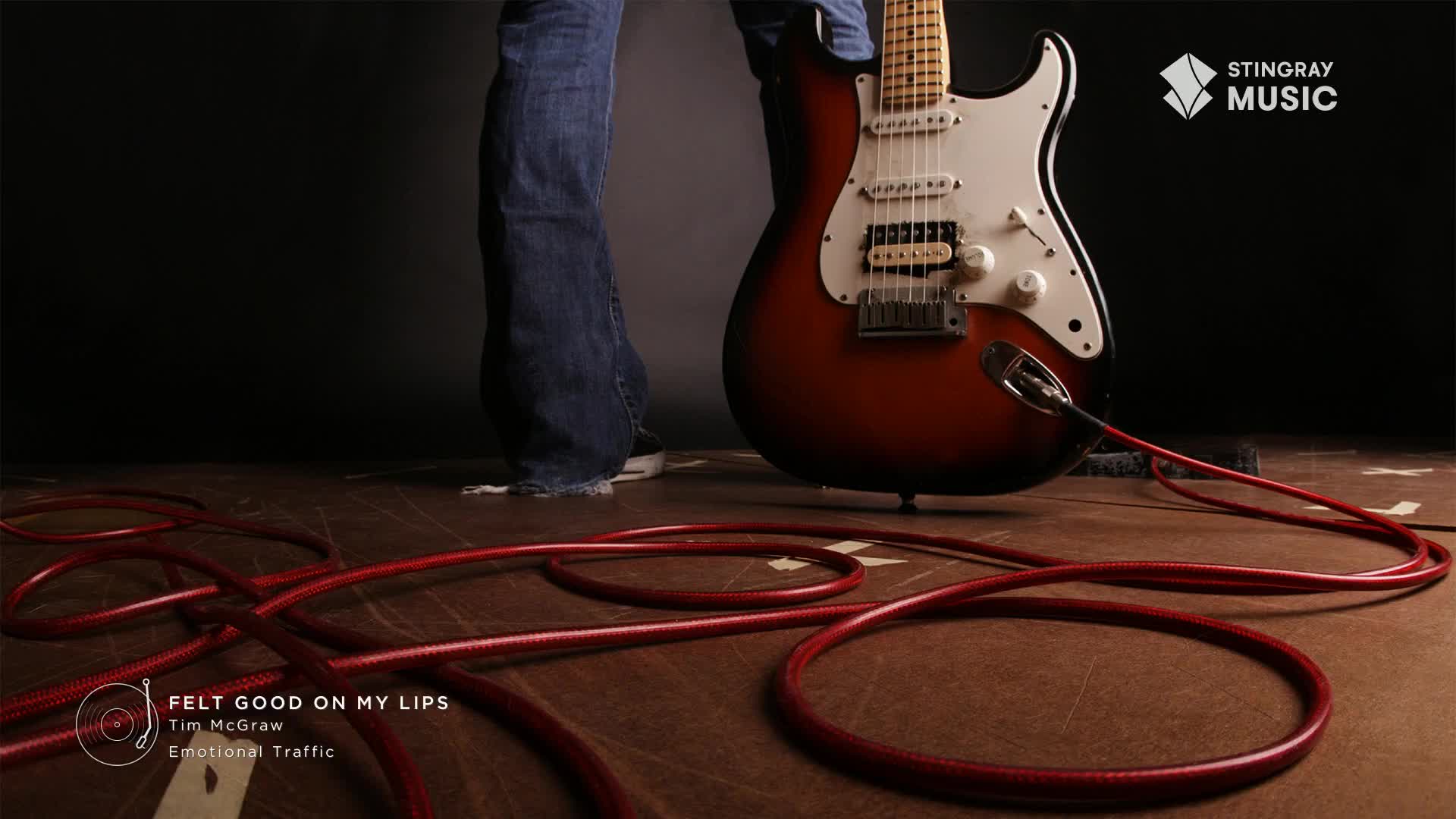 A sunburst electric guitar stands ready, its red cable coiled on the wooden floor.  The Stingray Hot Country logo is visible, hinting at a performance ready to begin.