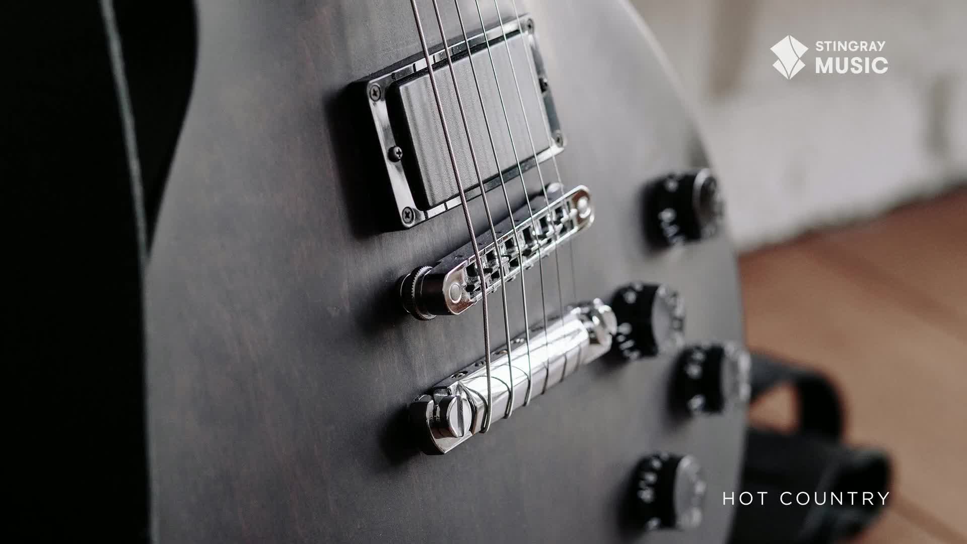 The matte black electric guitar gleams under the lights, its strings taut and ready. A logo for Stingray Music and the words "Hot Country" are visible.