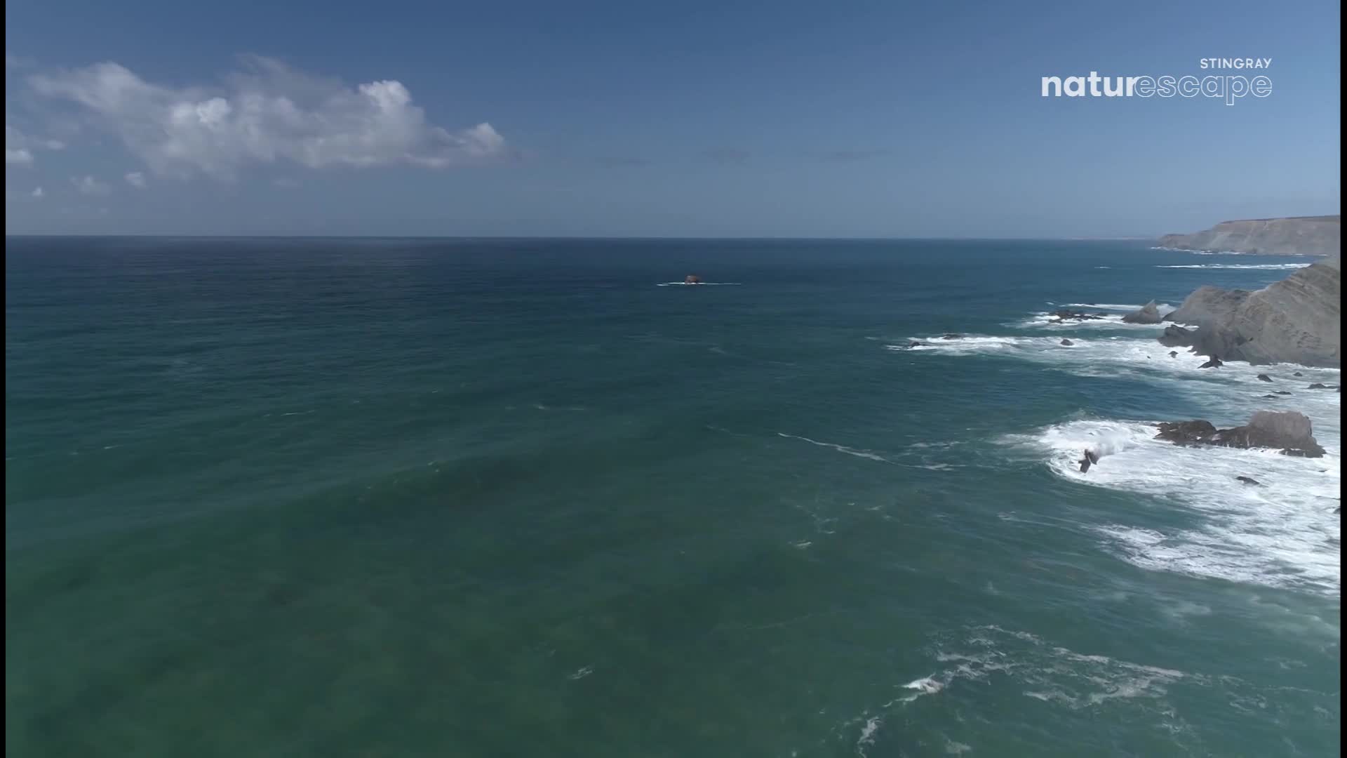 Waves crash against rugged cliffs along the Canadian coastline. A small, dark rock formation stands alone in the vast, blue ocean. Waves crash against rugged cliffs along the Canadian coastline. A small, dark rock formation stands alone in the vast, blue ocean.